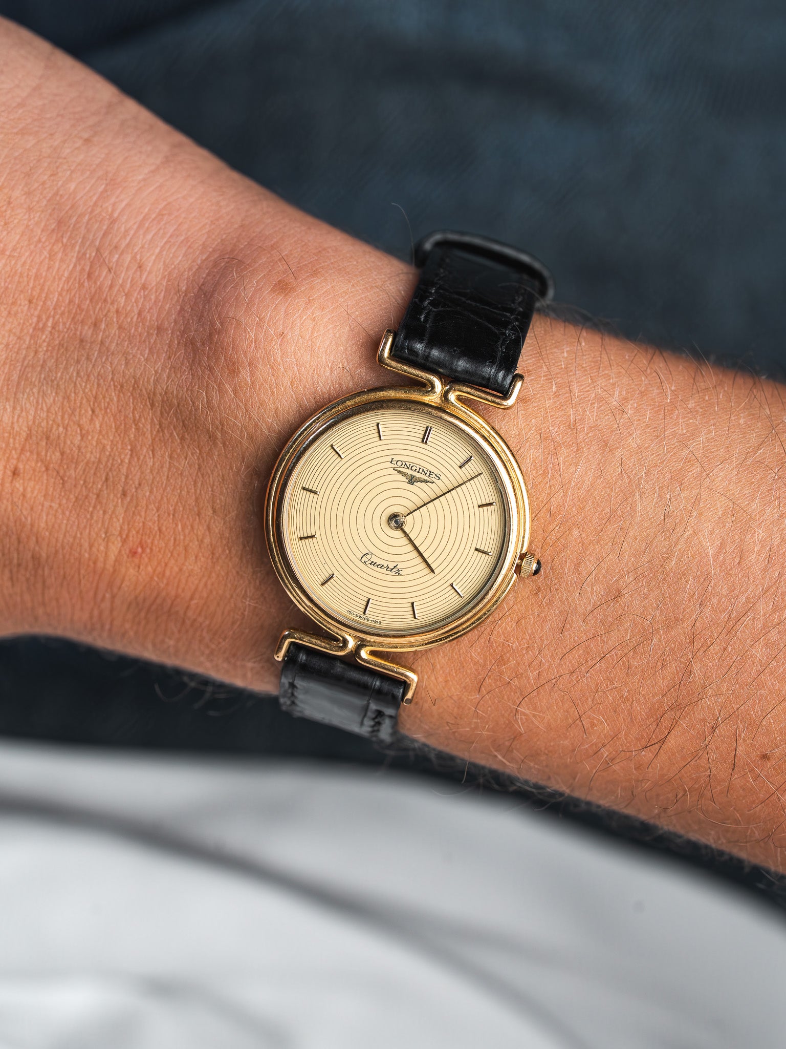 Longines vintage quartz watch with gold case, cream dial, black leather strap worn on wrist
