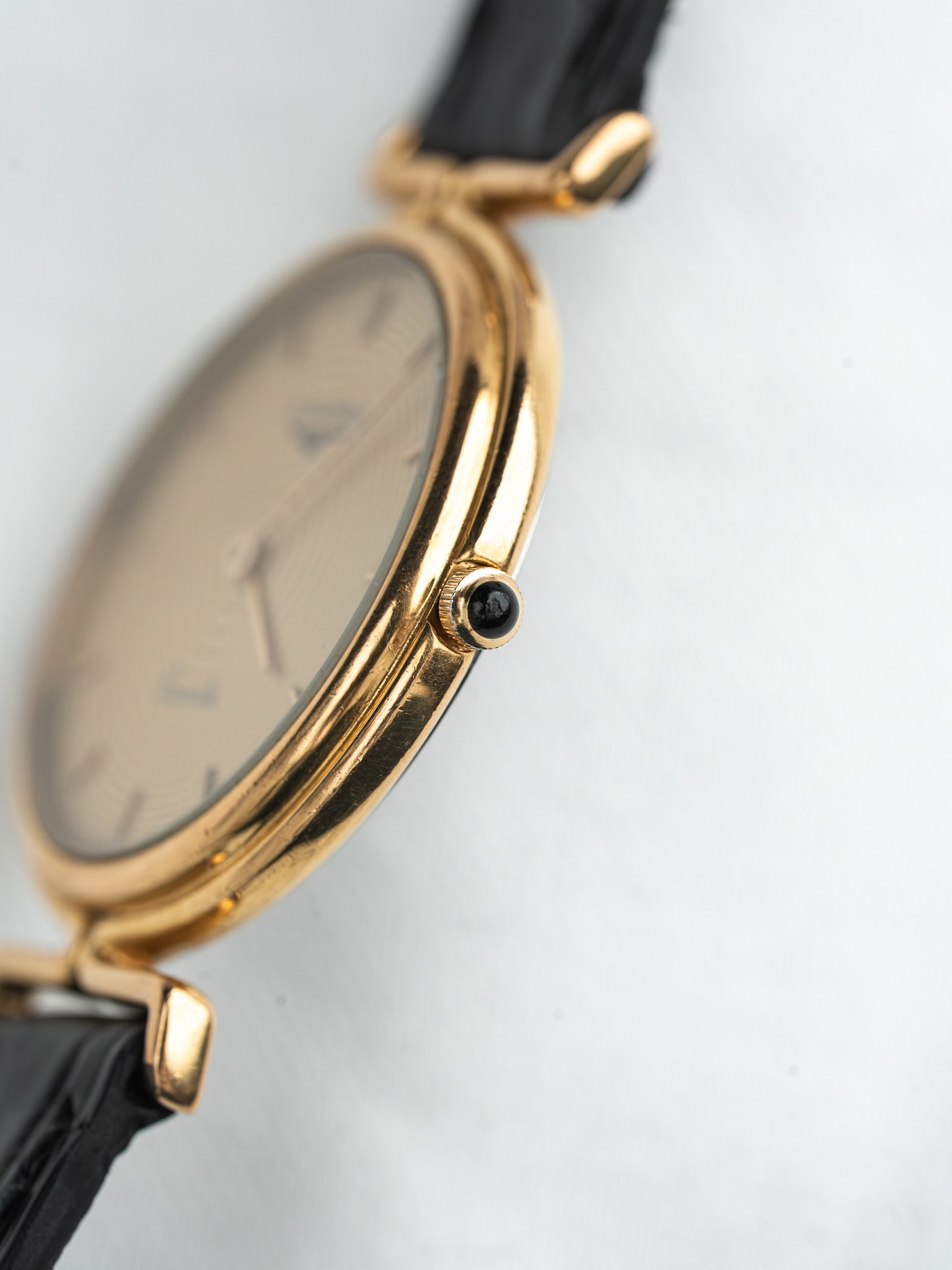 Vintage Cartier watch with gold case, black leather strap, and cream dial