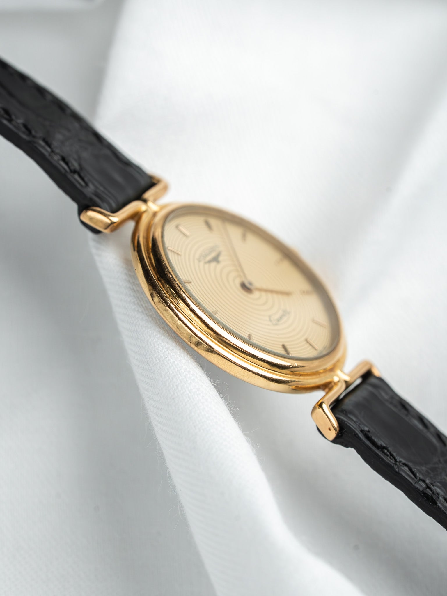 Vintage Universal Genève watch with gold case, cream dial, black leather strap on white fabric