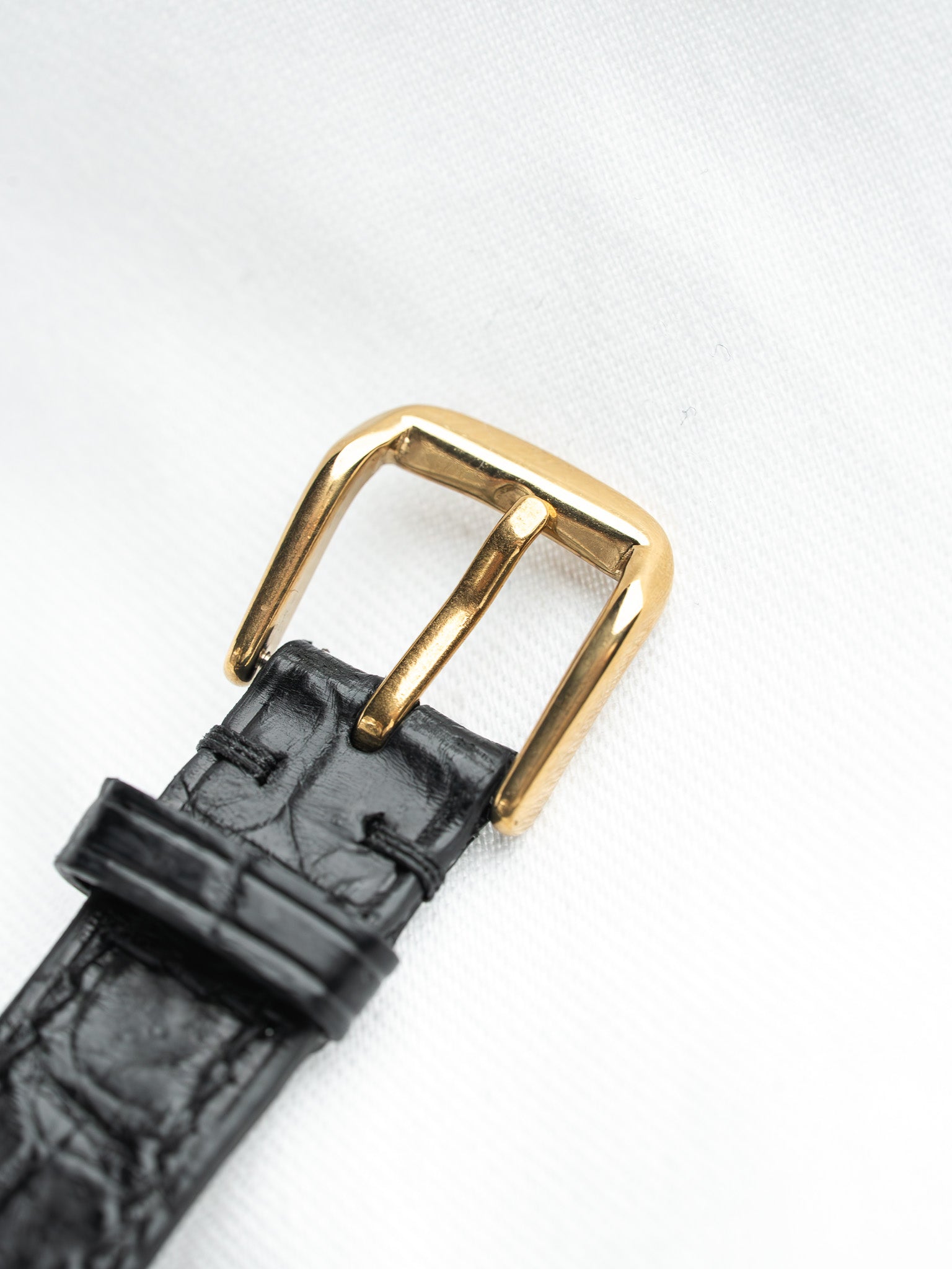 Black alligator leather watch strap with gold buckle on white background