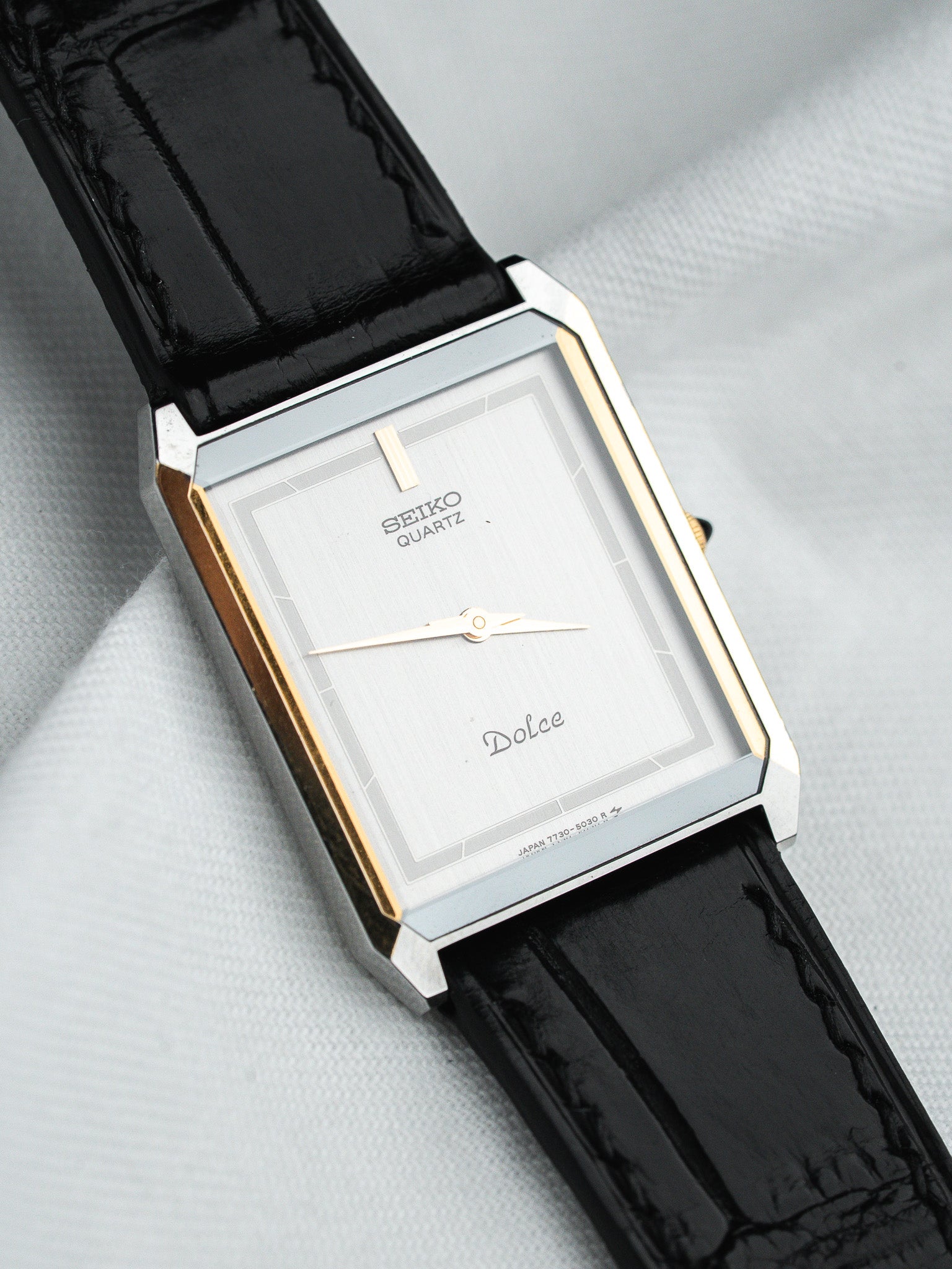 Seiko Dolce vintage quartz watch with silver dial, gold accents, black leather strap on white background