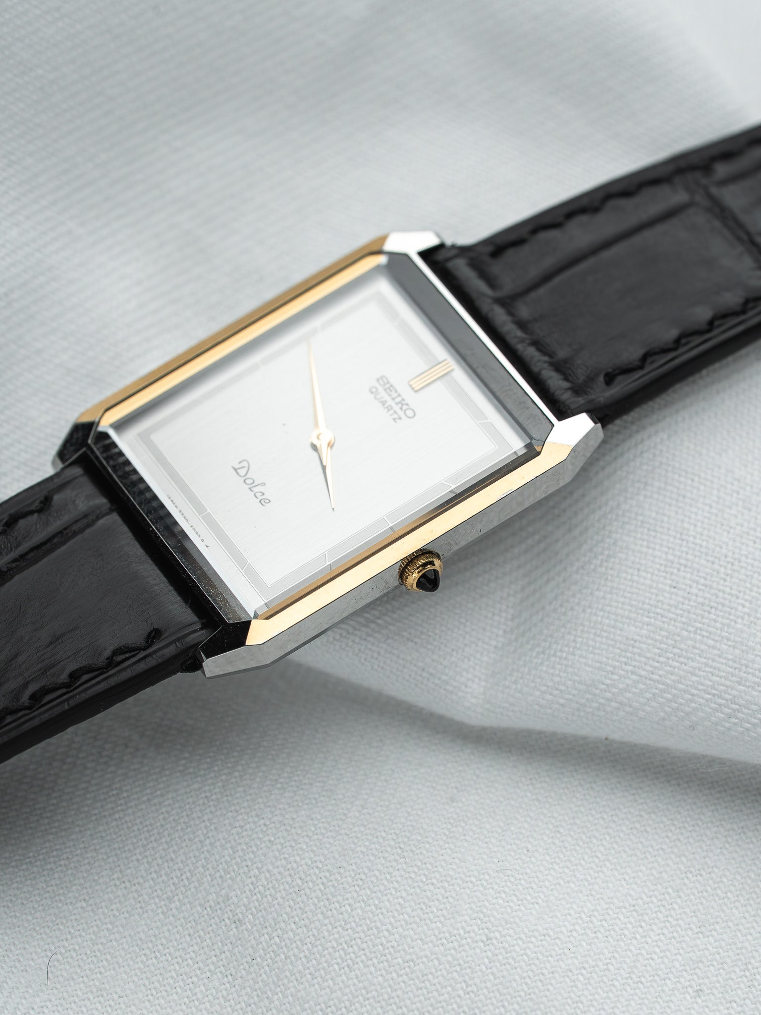 Seiko Dolce vintage watch with silver dial, gold accents, black leather strap on textured background