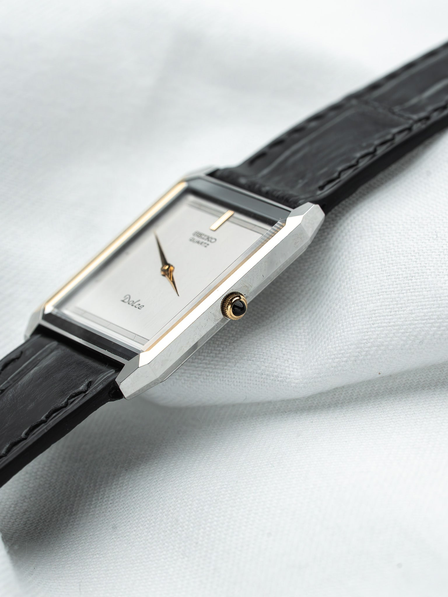 Seiko Dolce vintage watch with silver dial, gold accents, black leather strap on white fabric
