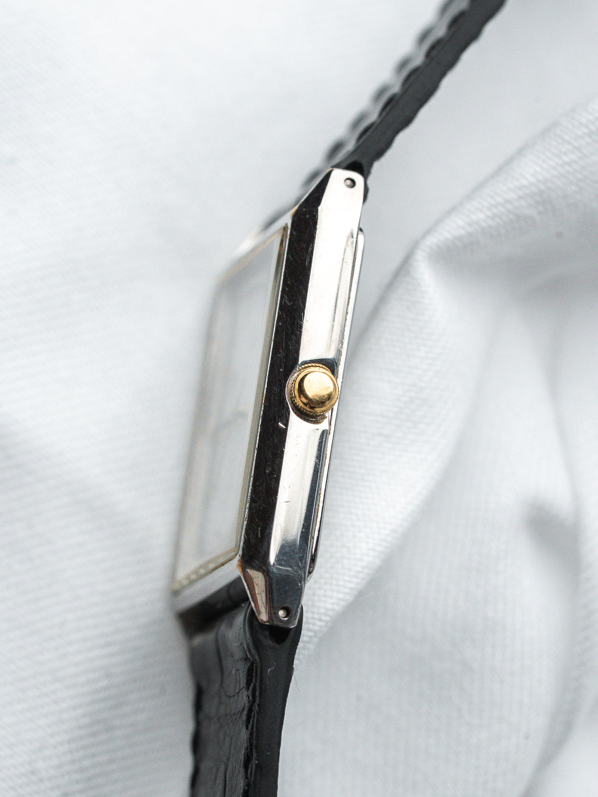 Cartier Tank montre vintage avec couronne dorée, bracelet en cuir noir, boîtier rectangulaire sur tissu blanc