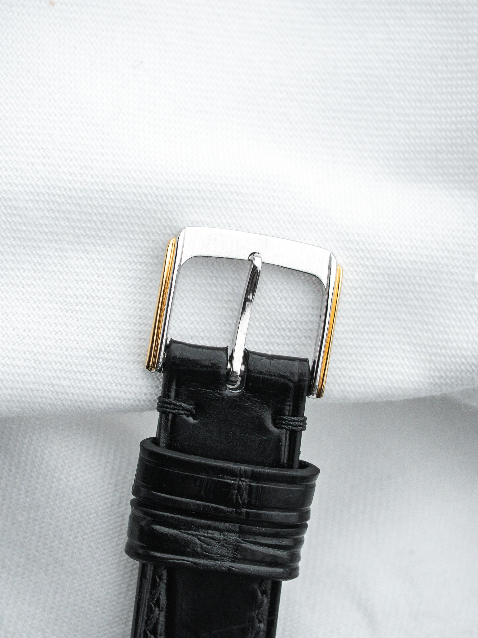 Black leather watch strap with two-tone buckle on white background