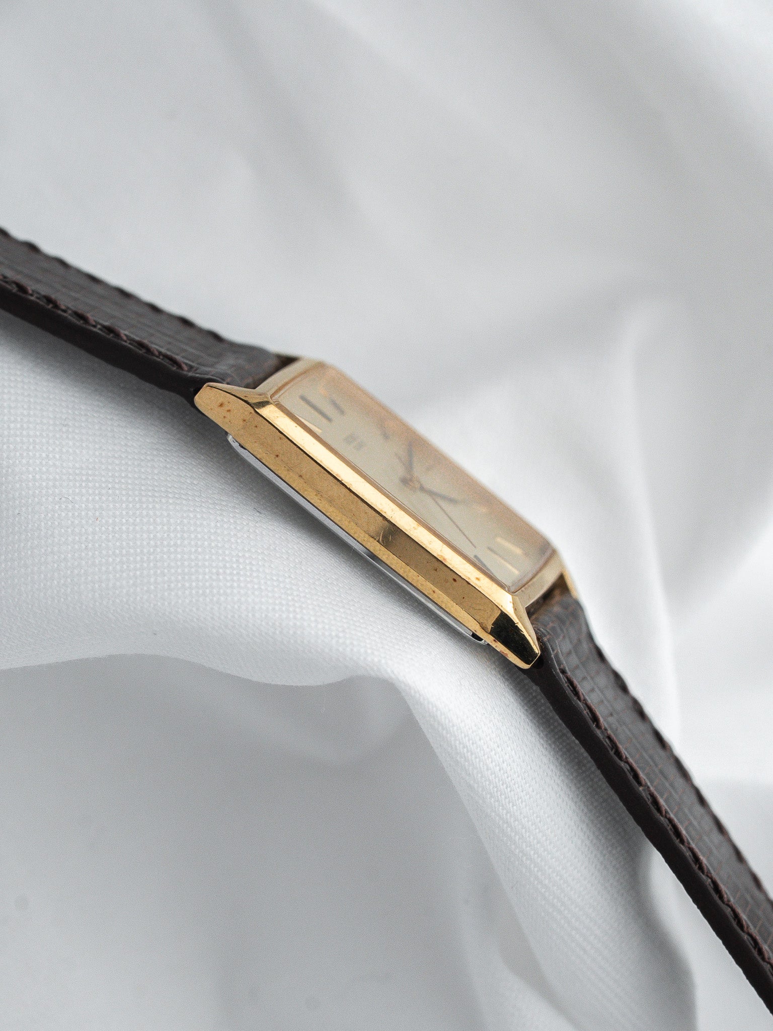 Vintage Cartier Tank watch with gold case, cream dial, brown leather strap on white fabric