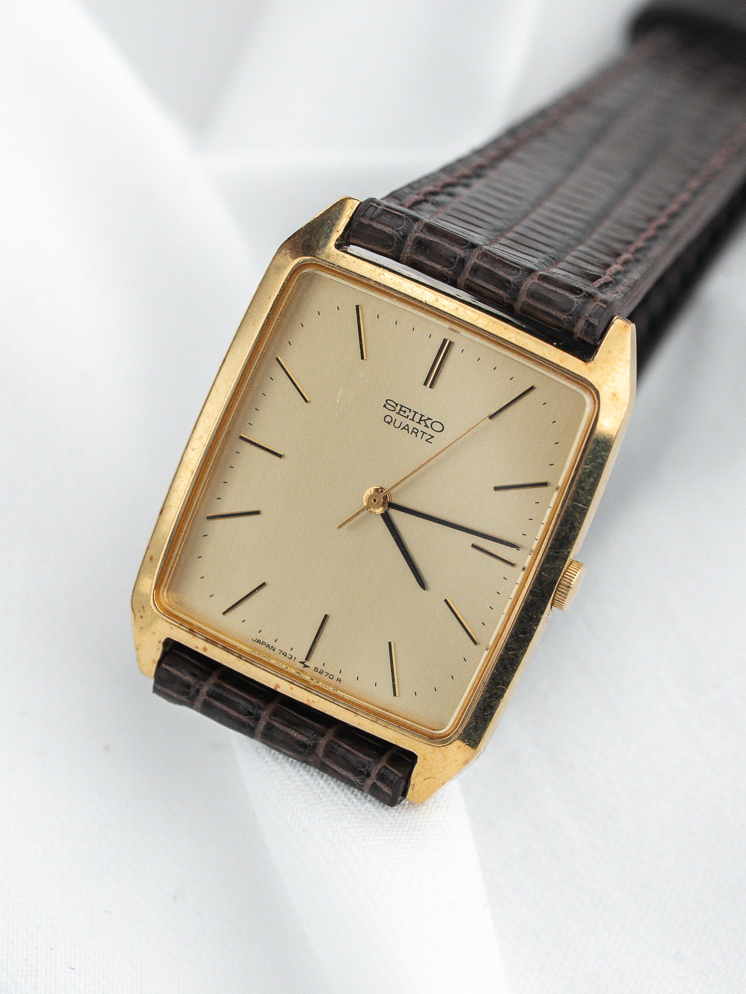 Vintage Seiko Quartz watch with gold case, cream dial, and brown leather strap on white background