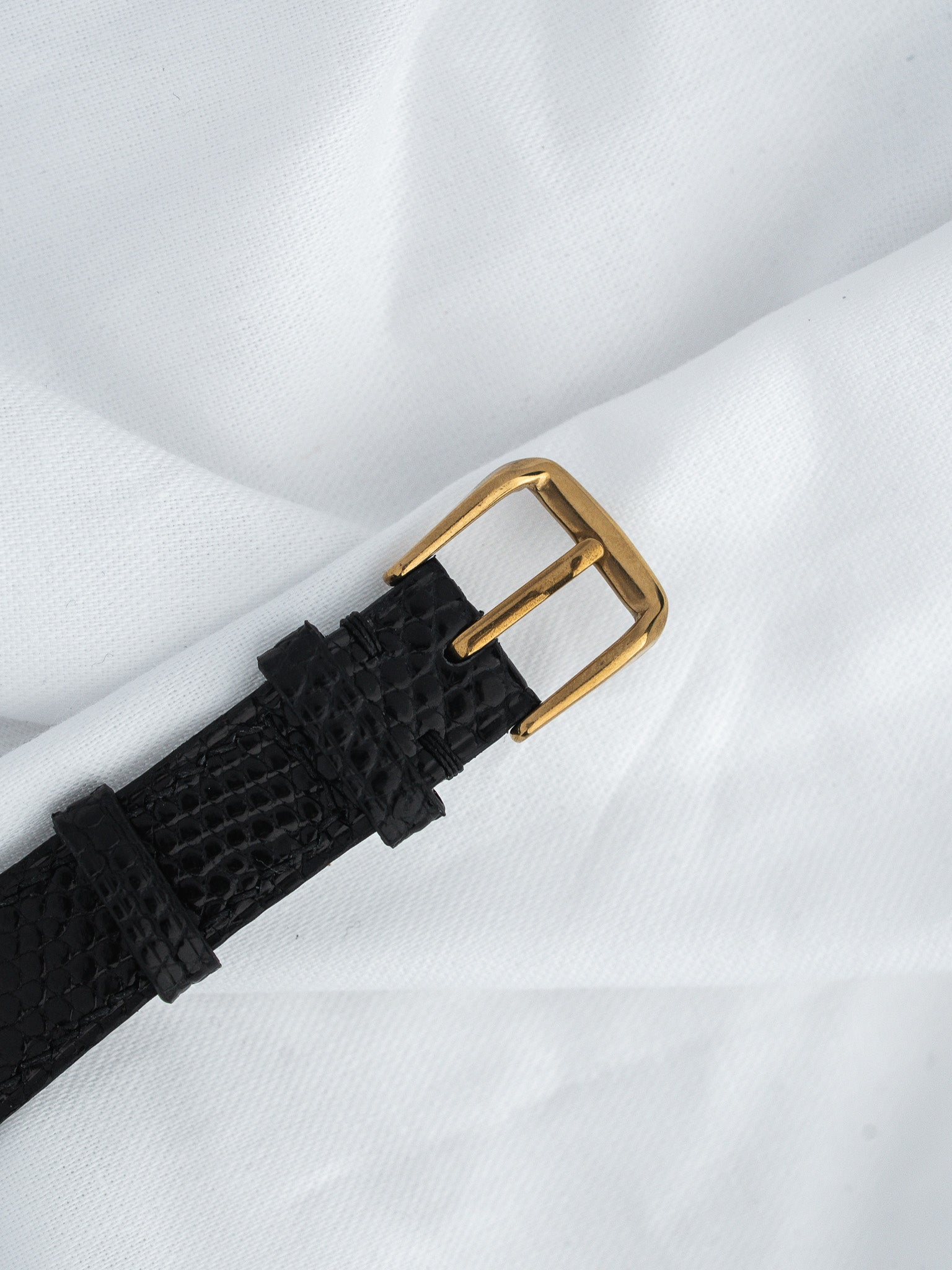 Black textured leather strap with gold buckle on white fabric