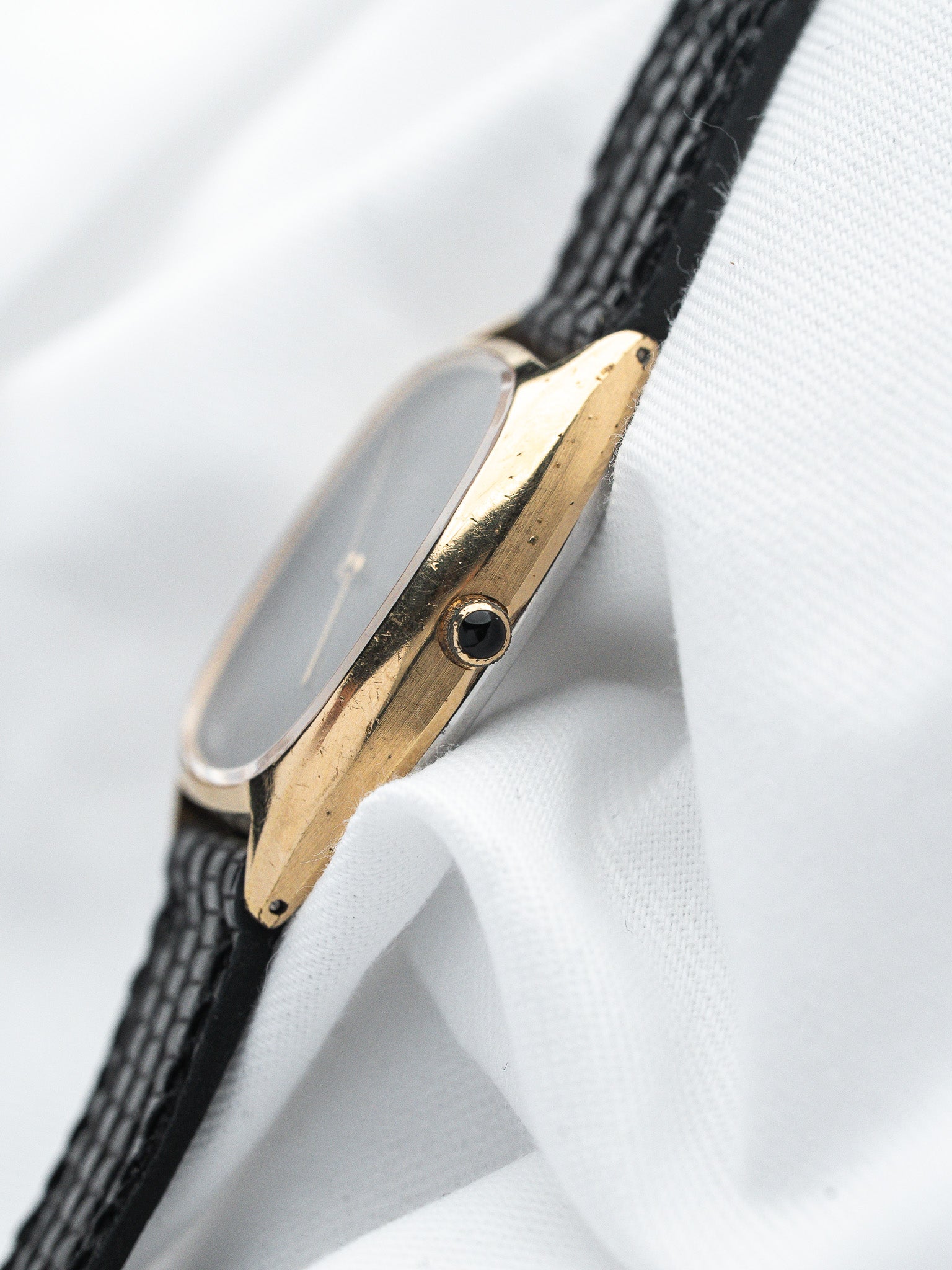 Vintage watch with gold case, black strap, and minimalist dial on white fabric