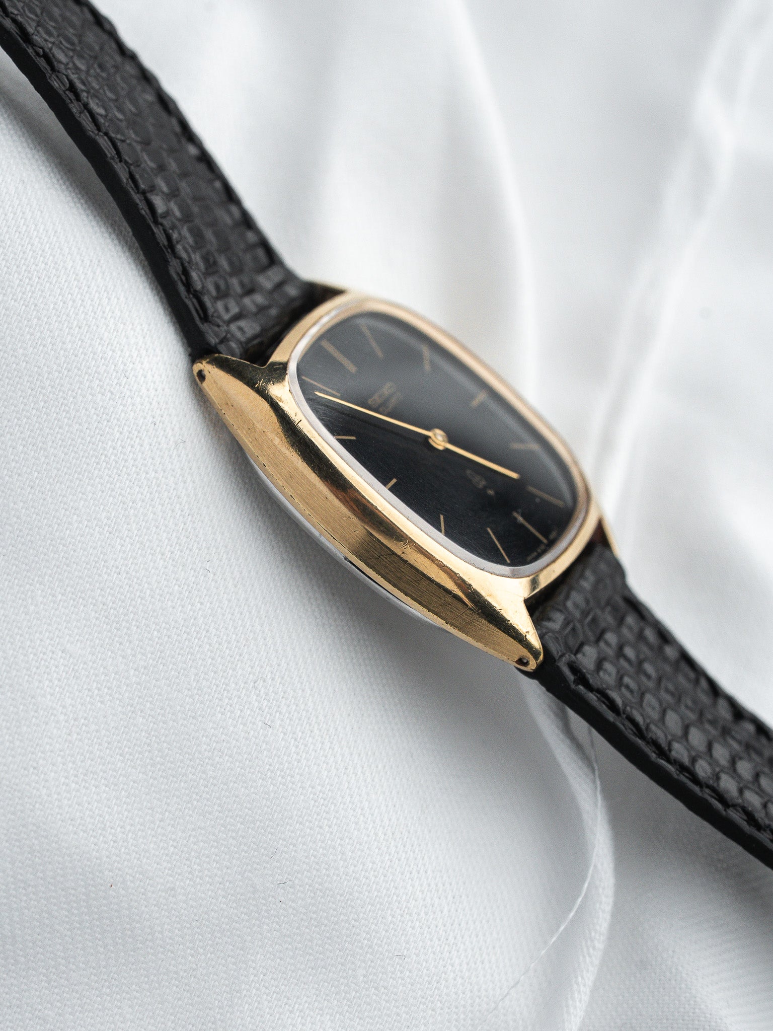 Vintage Omega watch with gold case, black dial, and textured leather strap