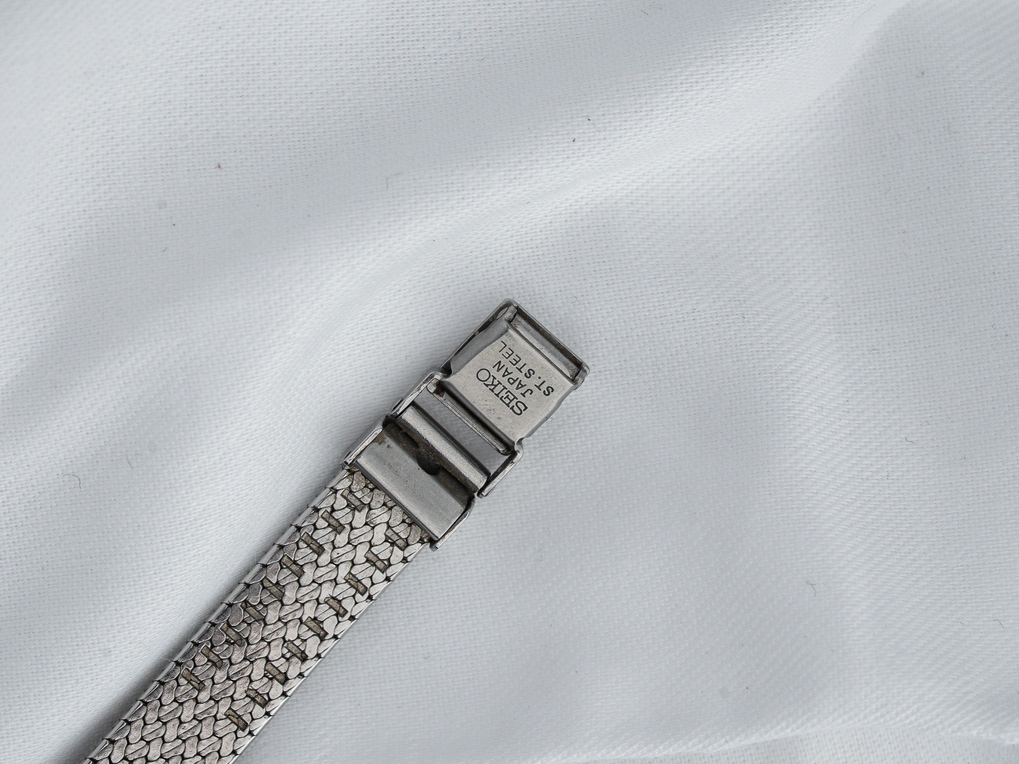 Seiko vintage watch bracelet with mesh design and steel clasp on white fabric