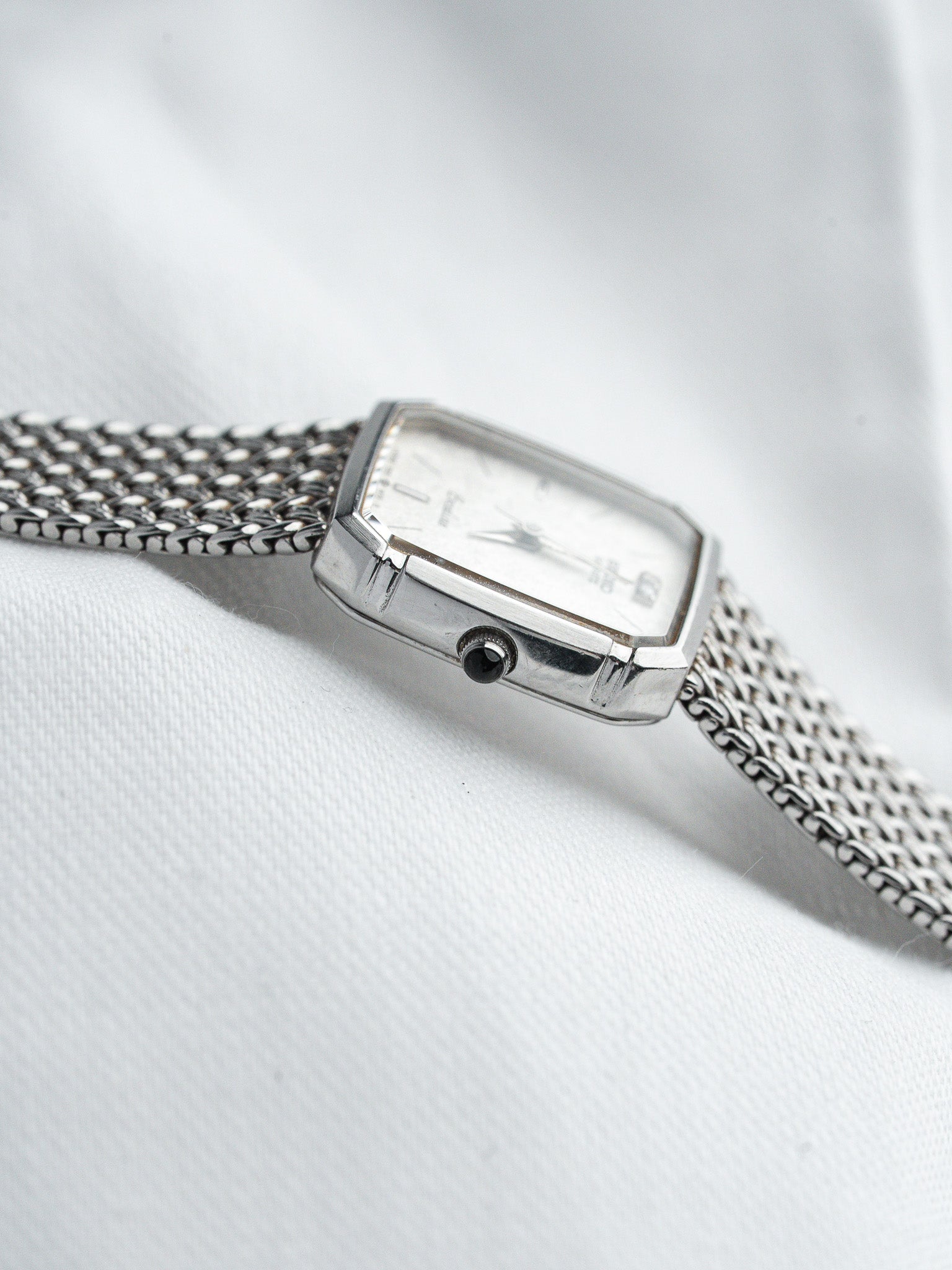 Vintage Omega rectangular watch with silver mesh bracelet on white fabric