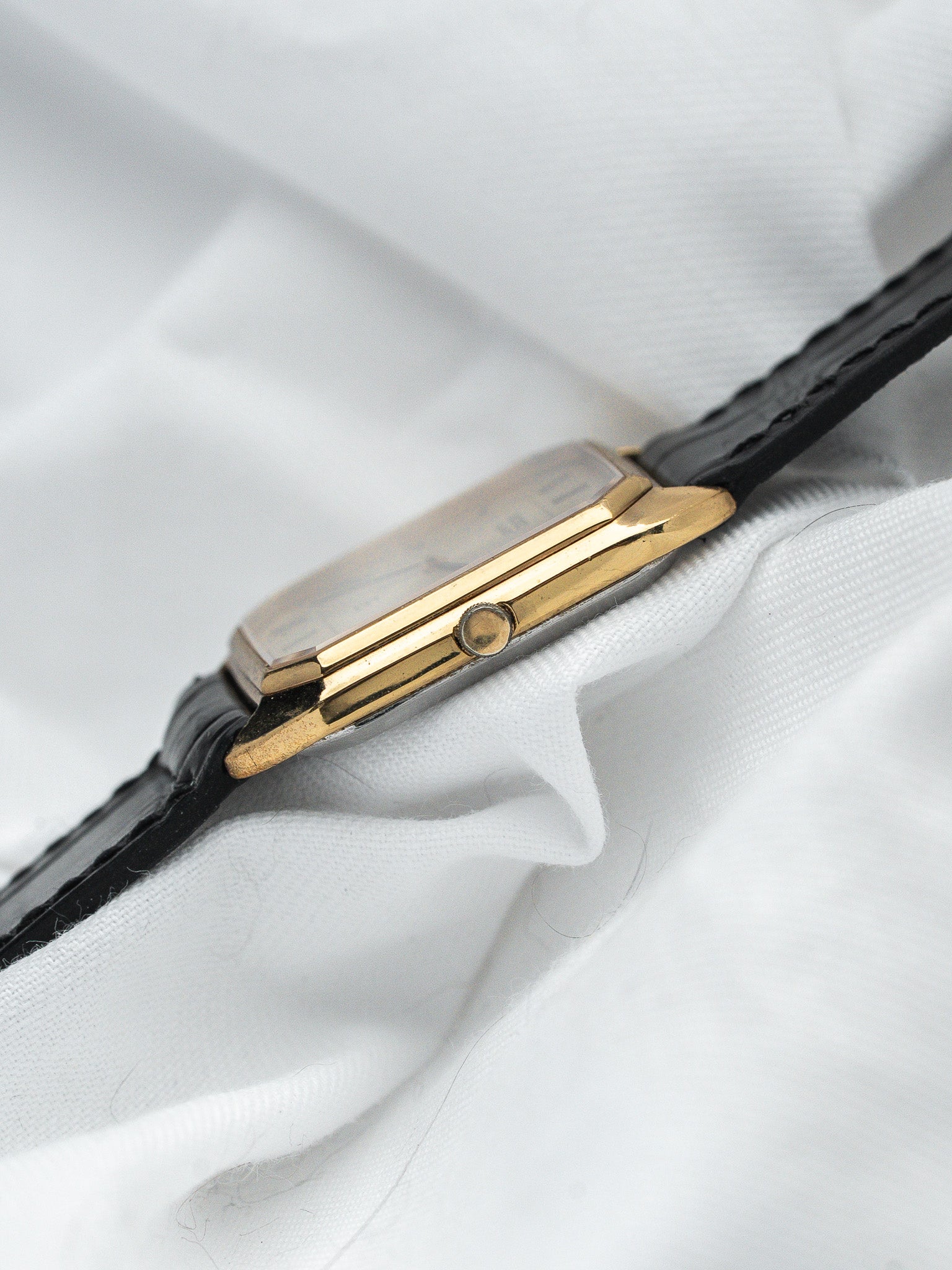 Vintage Cartier watch with gold case and black leather strap on white fabric