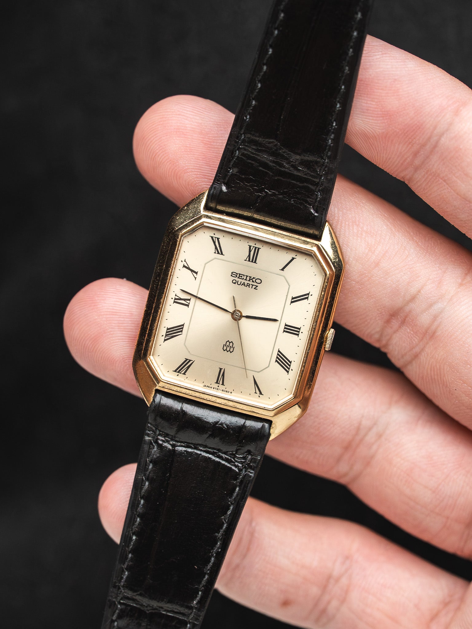 Seiko Quartz vintage watch with gold case, cream dial, Roman numerals, black leather strap held in hand