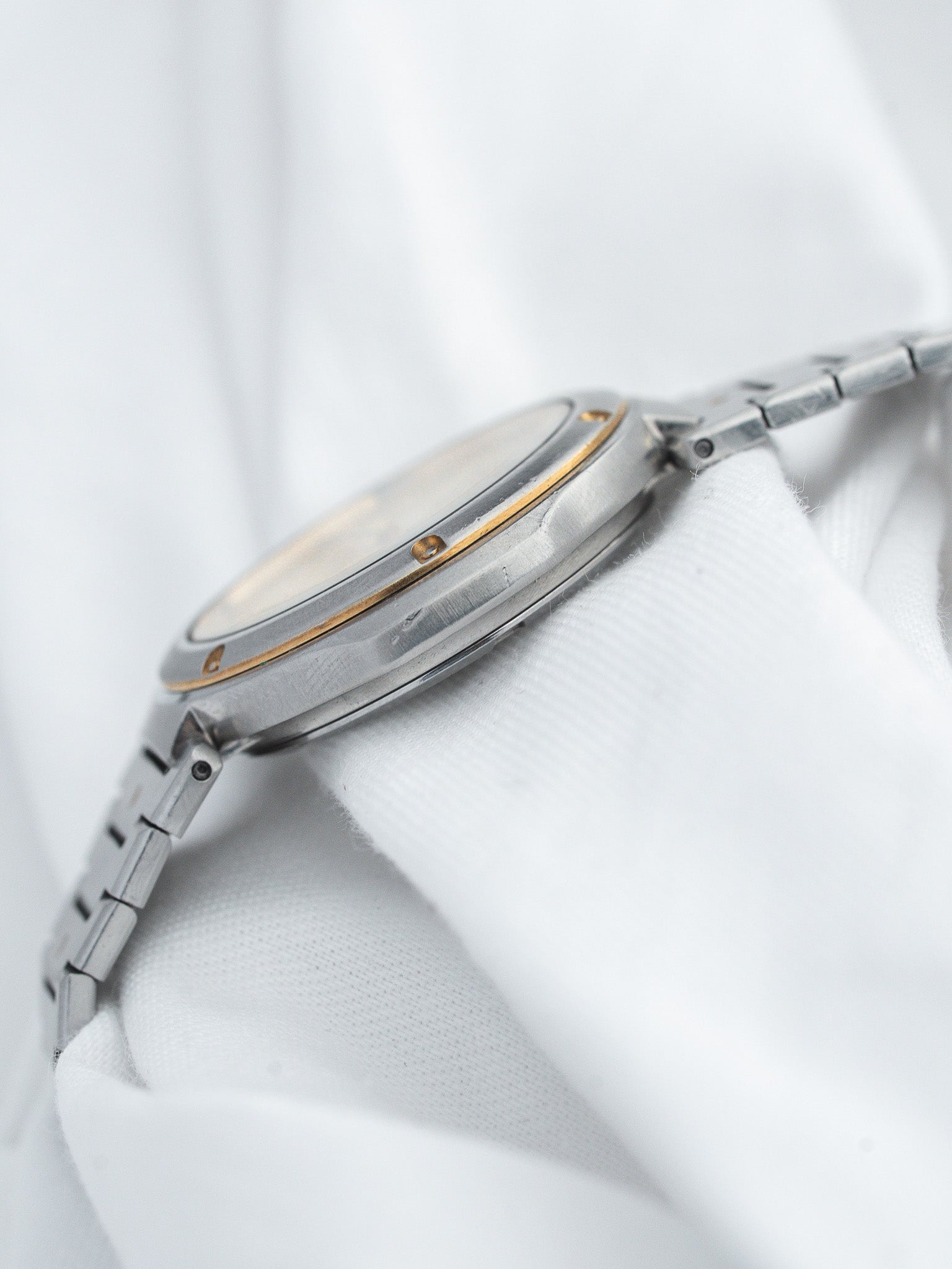 Vintage Omega watch with steel case, gold accents, and metal bracelet on white fabric