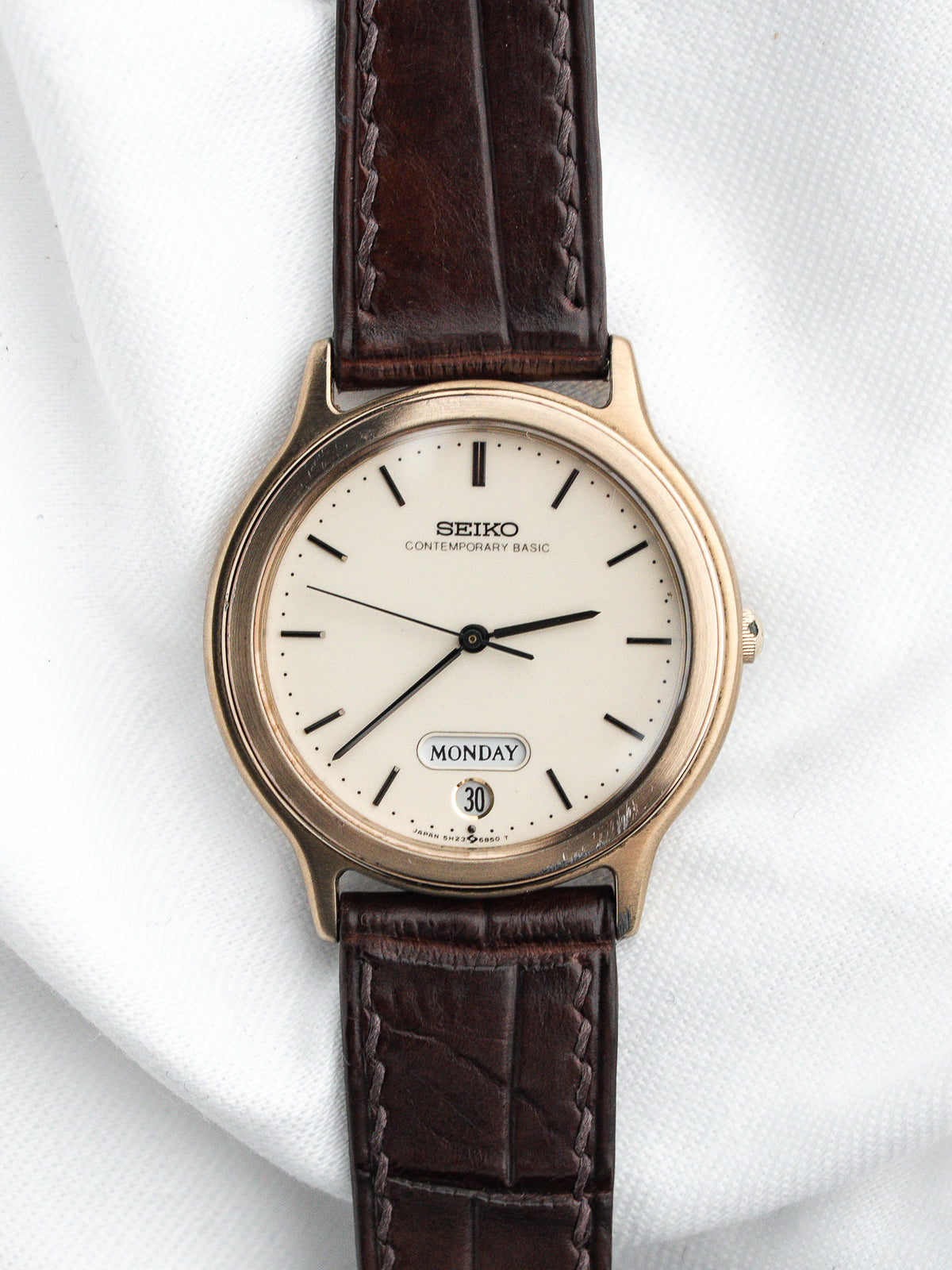 Montre Seiko vintage avec cadran blanc, boîtier doré et bracelet en cuir marron.