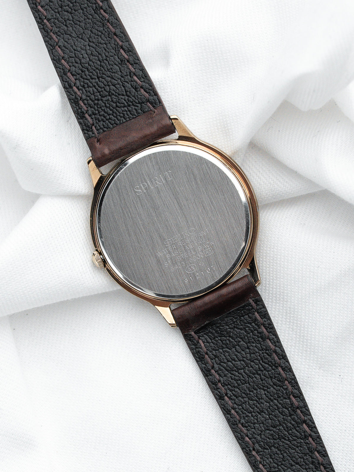 Dos d'une montre Spirit avec boîtier doré et bracelet en cuir noir grainé.
