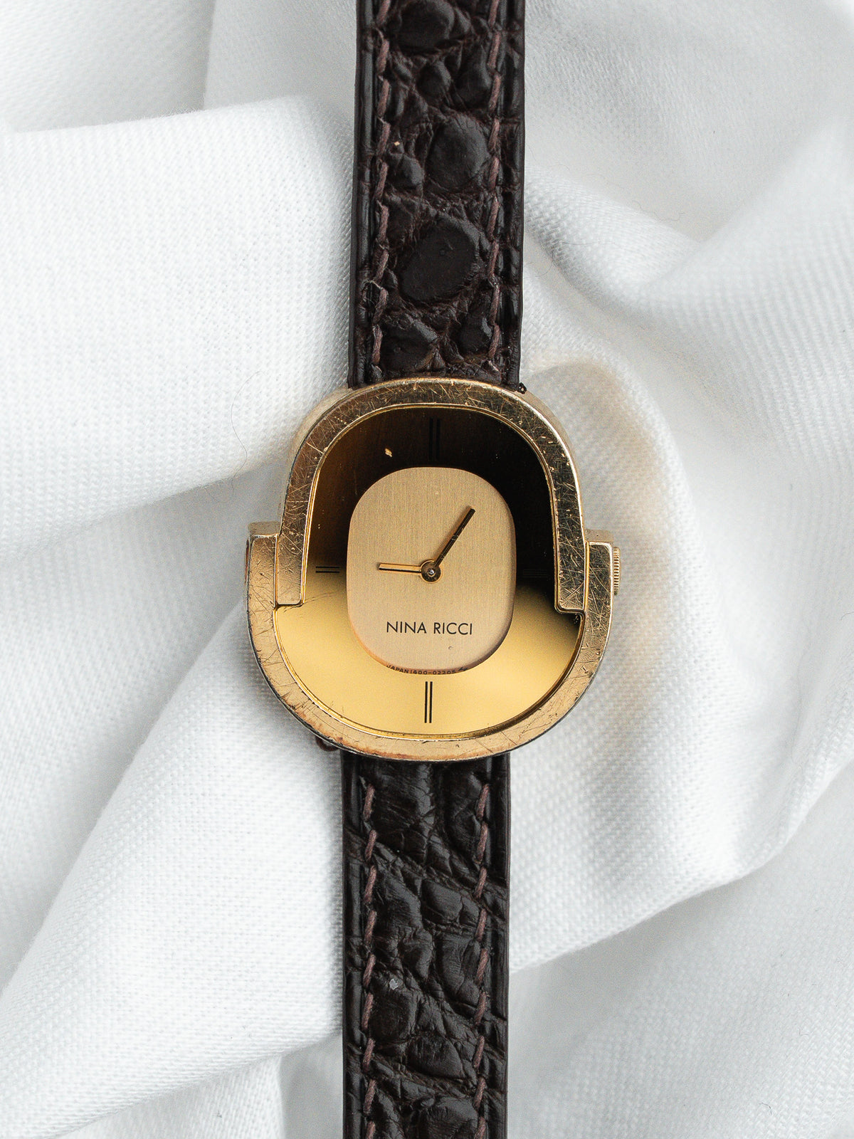Montre Nina Ricci vintage dorée avec cadran ovale et bracelet en cuir marron.