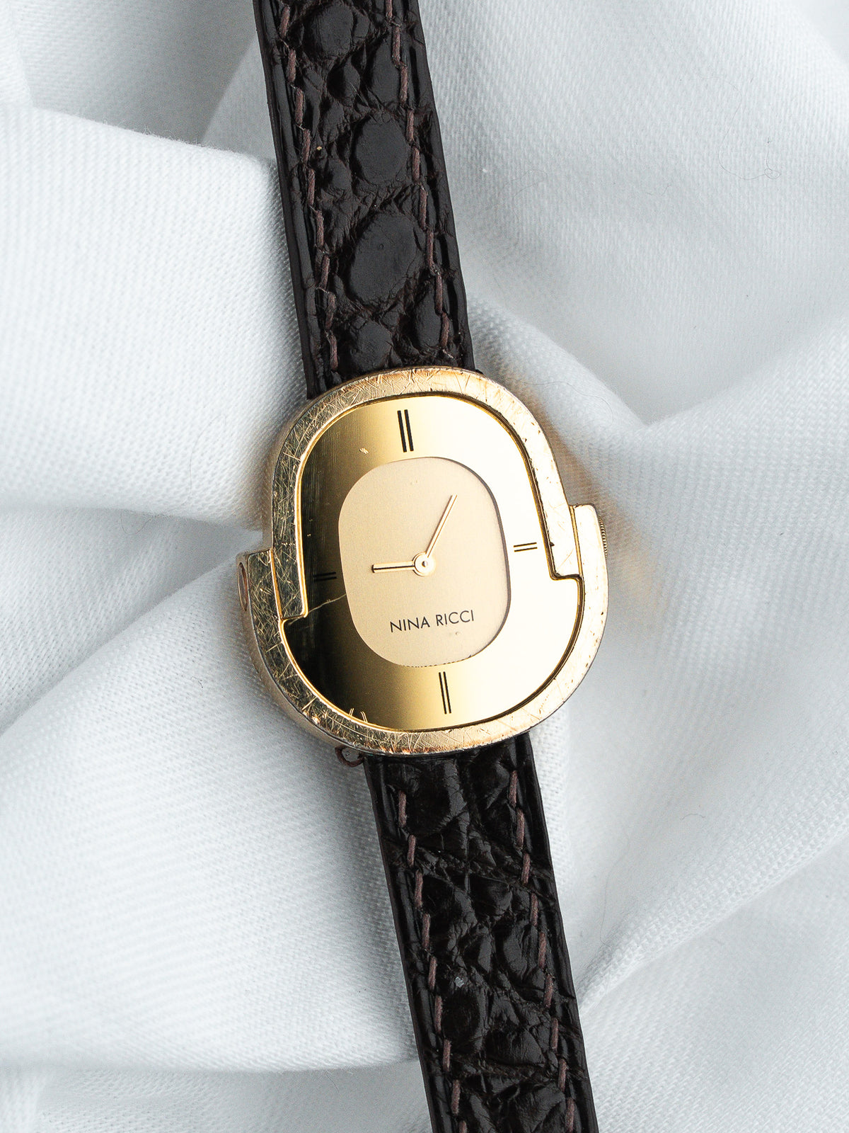 Montre Nina Ricci vintage avec boîtier doré et bracelet en cuir noir texturé.
