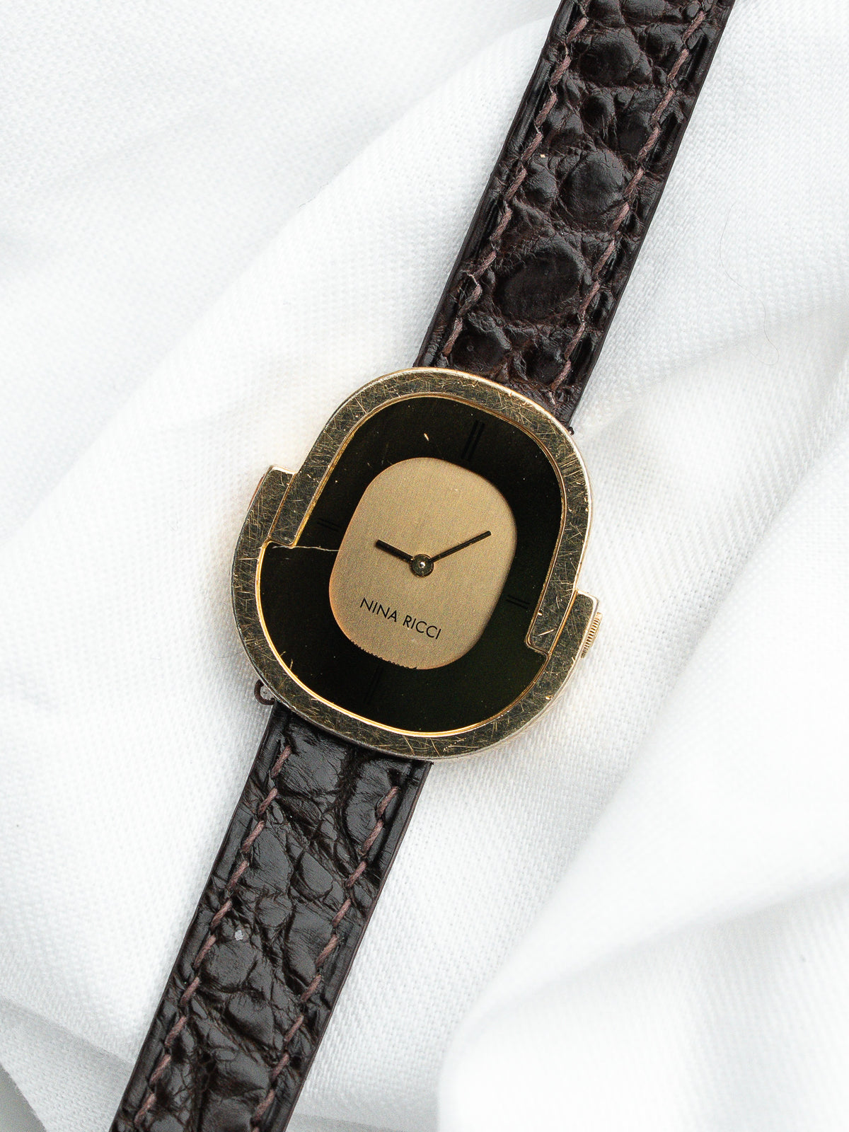 Montre Nina Ricci vintage au boîtier doré et bracelet en cuir marron texturé.