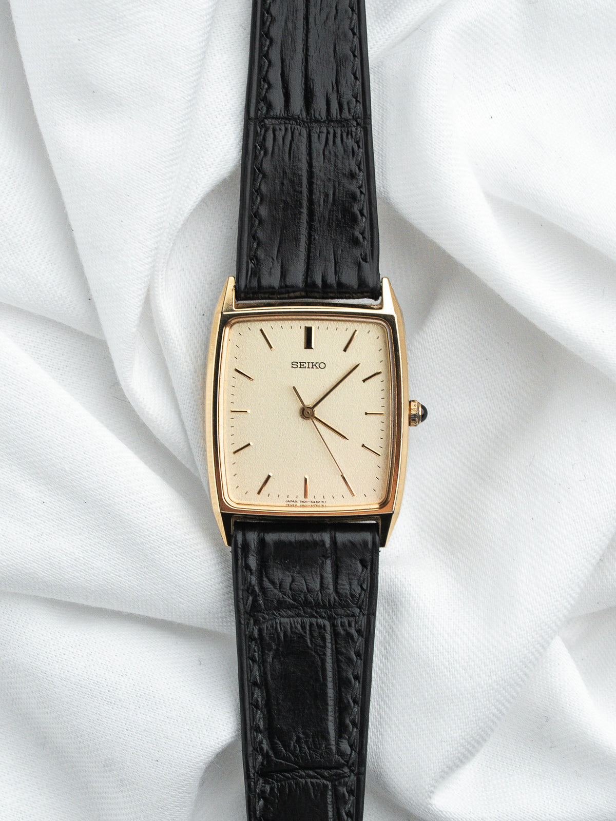 Montre Seiko vintage rectangulaire en or avec bracelet en cuir noir grainé.