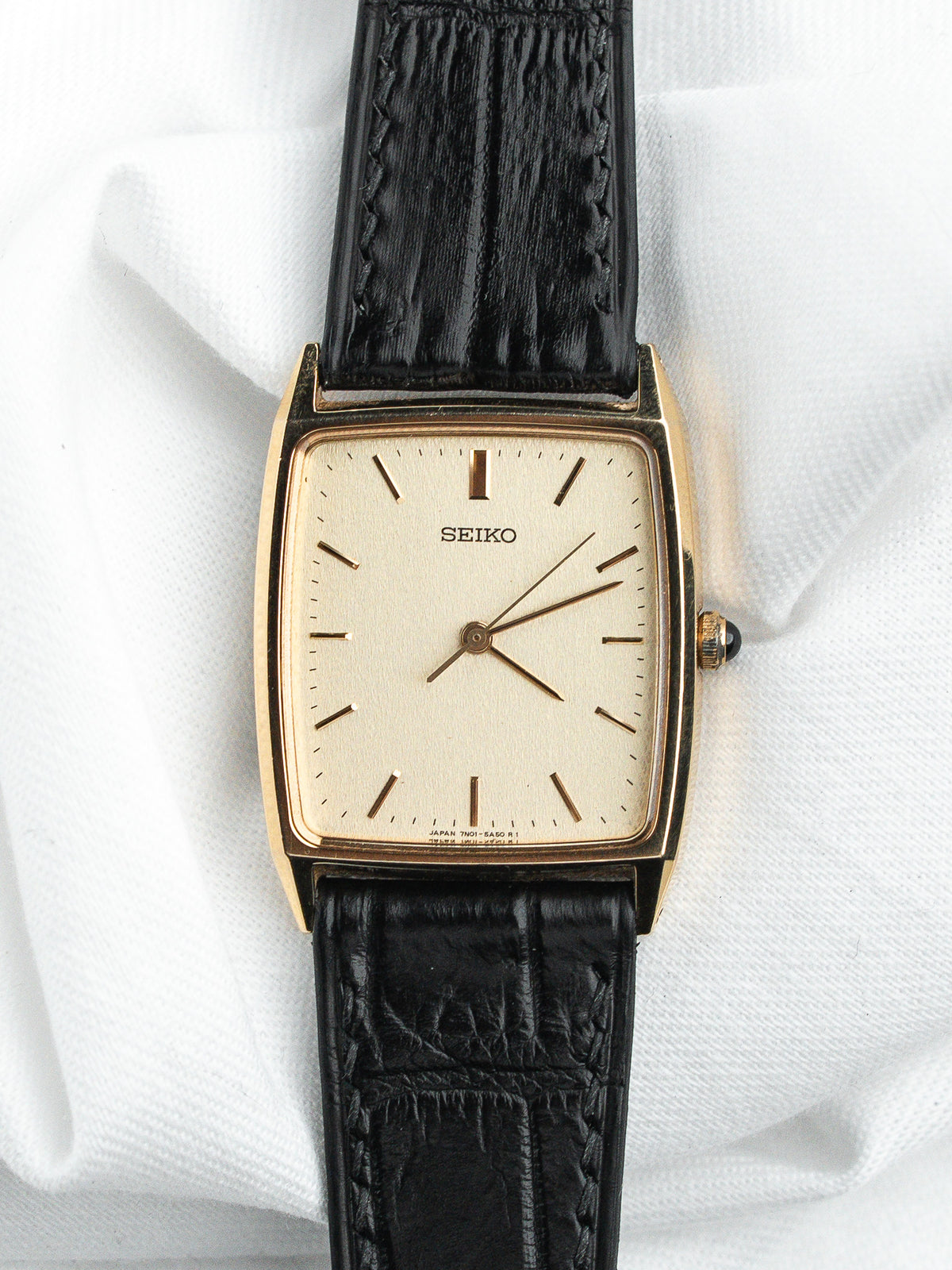 Montre Seiko vintage avec boîtier rectangulaire doré, cadran champagne et bracelet en cuir noir.