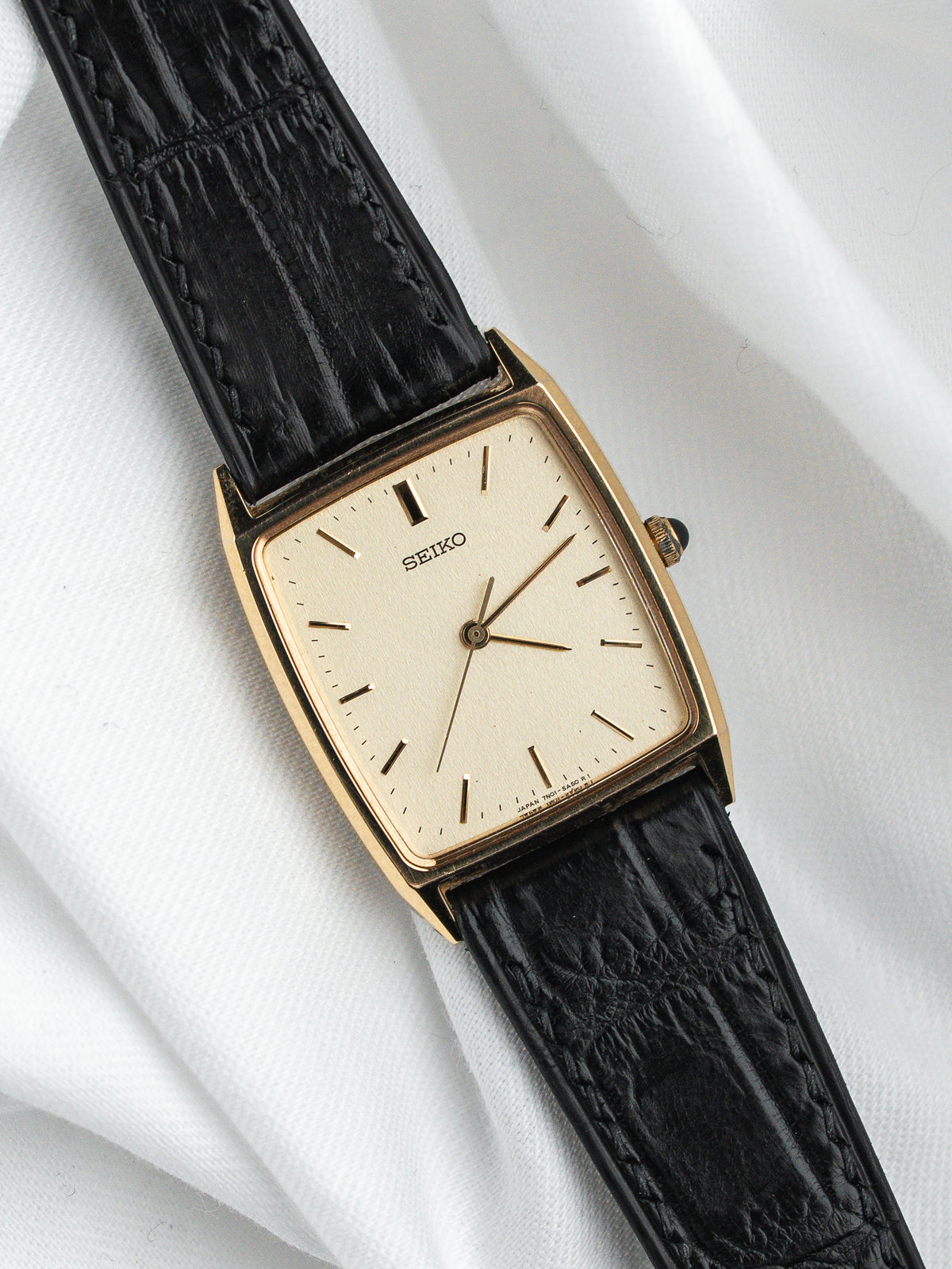 Montre Seiko vintage au boîtier rectangulaire doré et bracelet en cuir noir grainé.