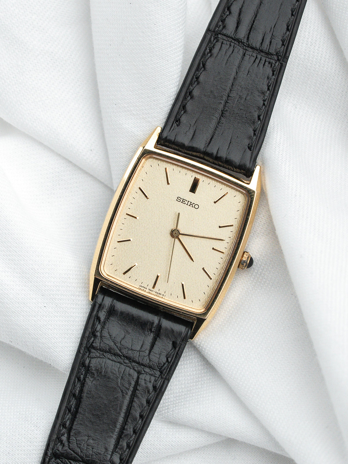 Montre Seiko vintage rectangulaire avec cadran doré et bracelet en cuir noir grainé.