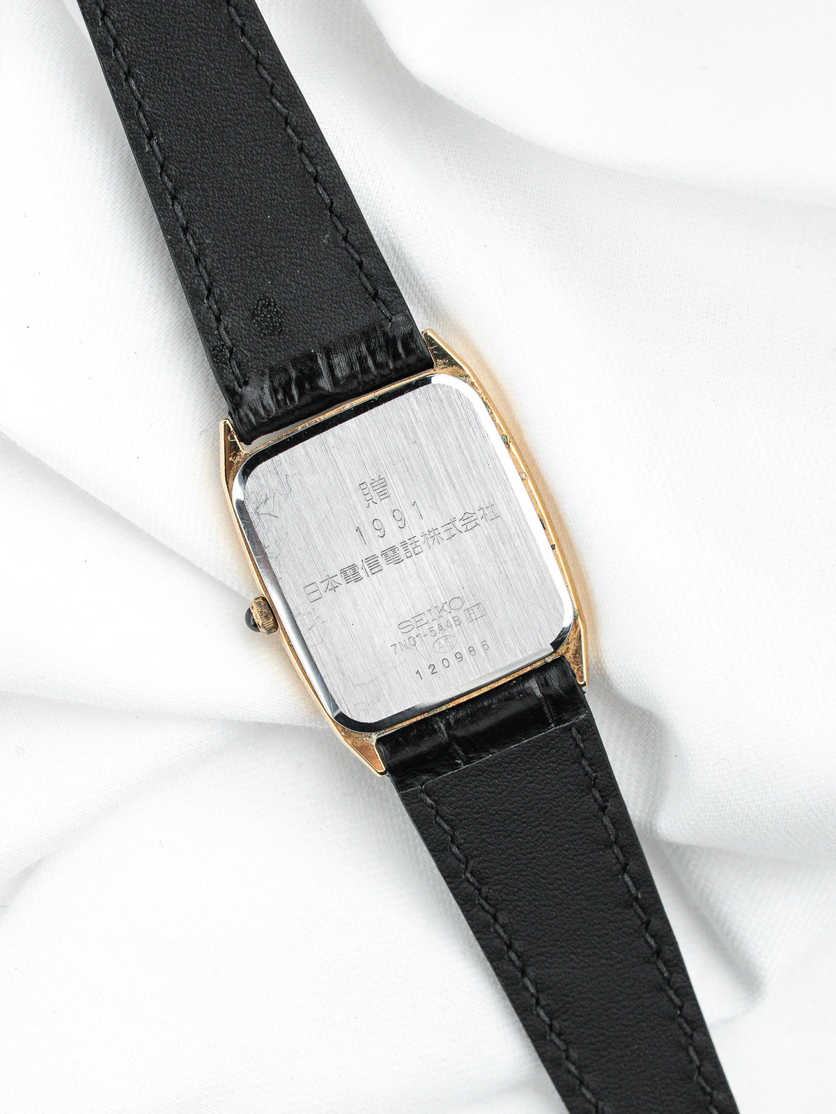 Dos d'une montre Seiko vintage rectangulaire dorée avec un bracelet en cuir noir.