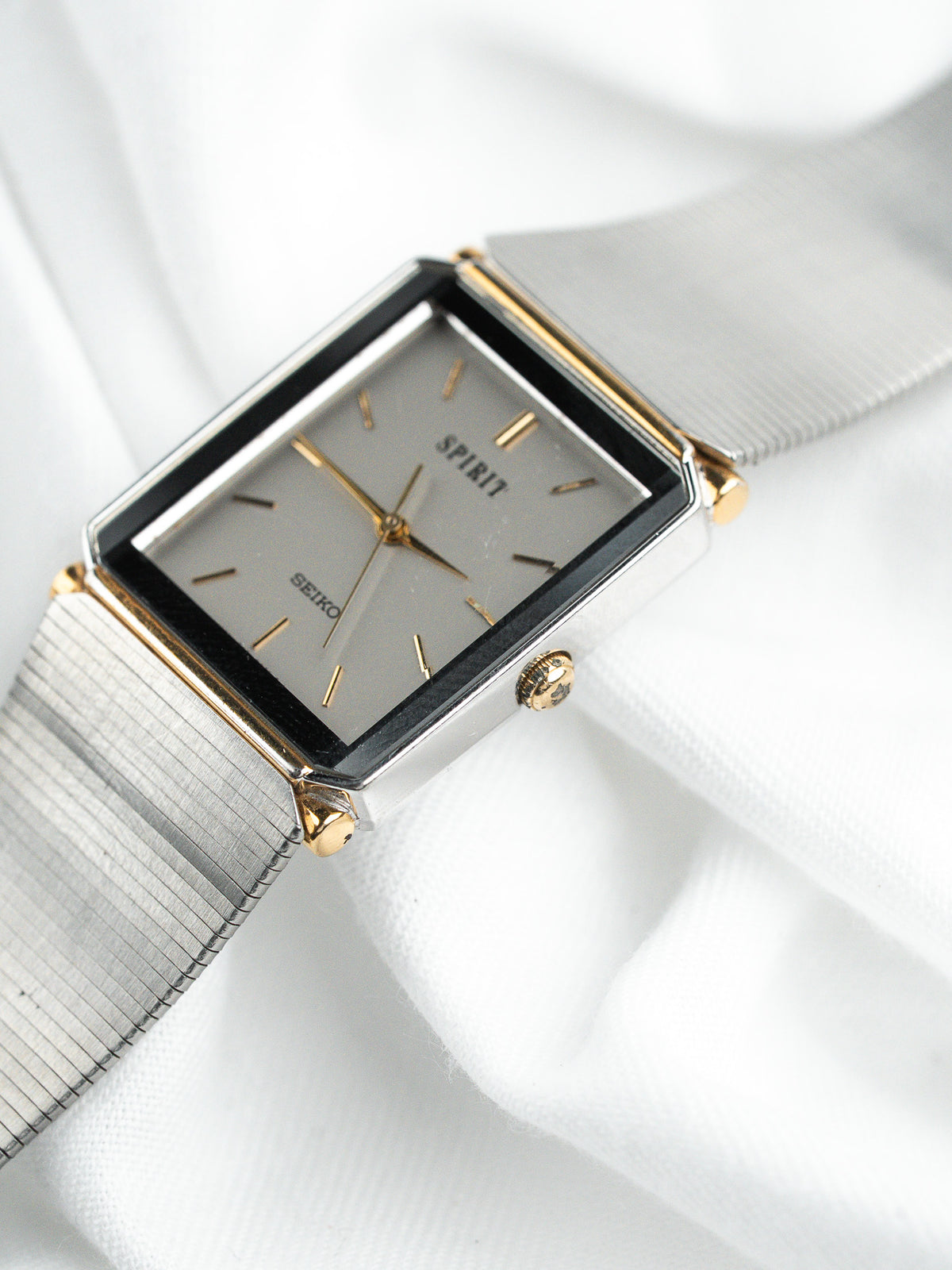 Montre Seiko Spirit vintage rectangulaire avec bracelet en maille argentée sur tissu blanc.