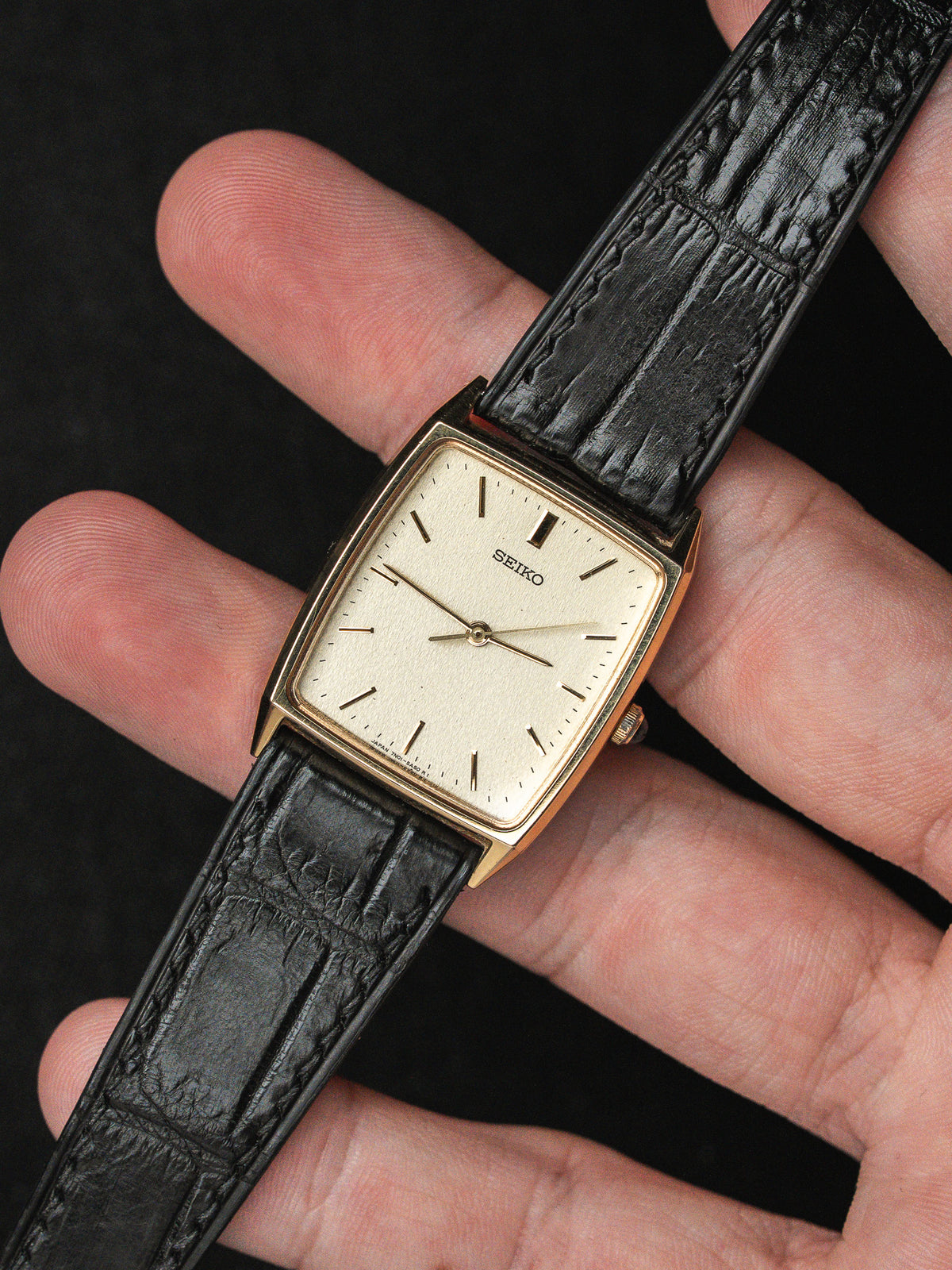 Montre Seiko vintage à boîtier rectangulaire doré avec cadran blanc et bracelet en cuir noir.