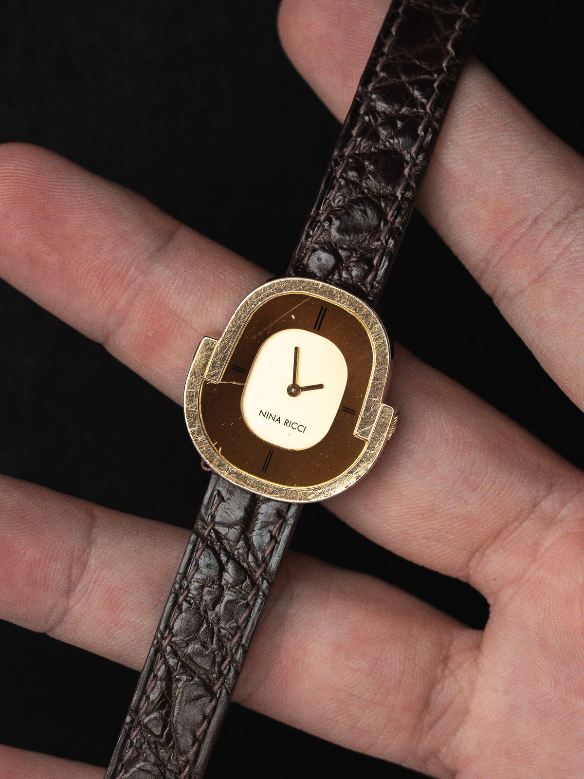 Montre Nina Ricci vintage avec boîtier doré et bracelet en cuir marron texturé.