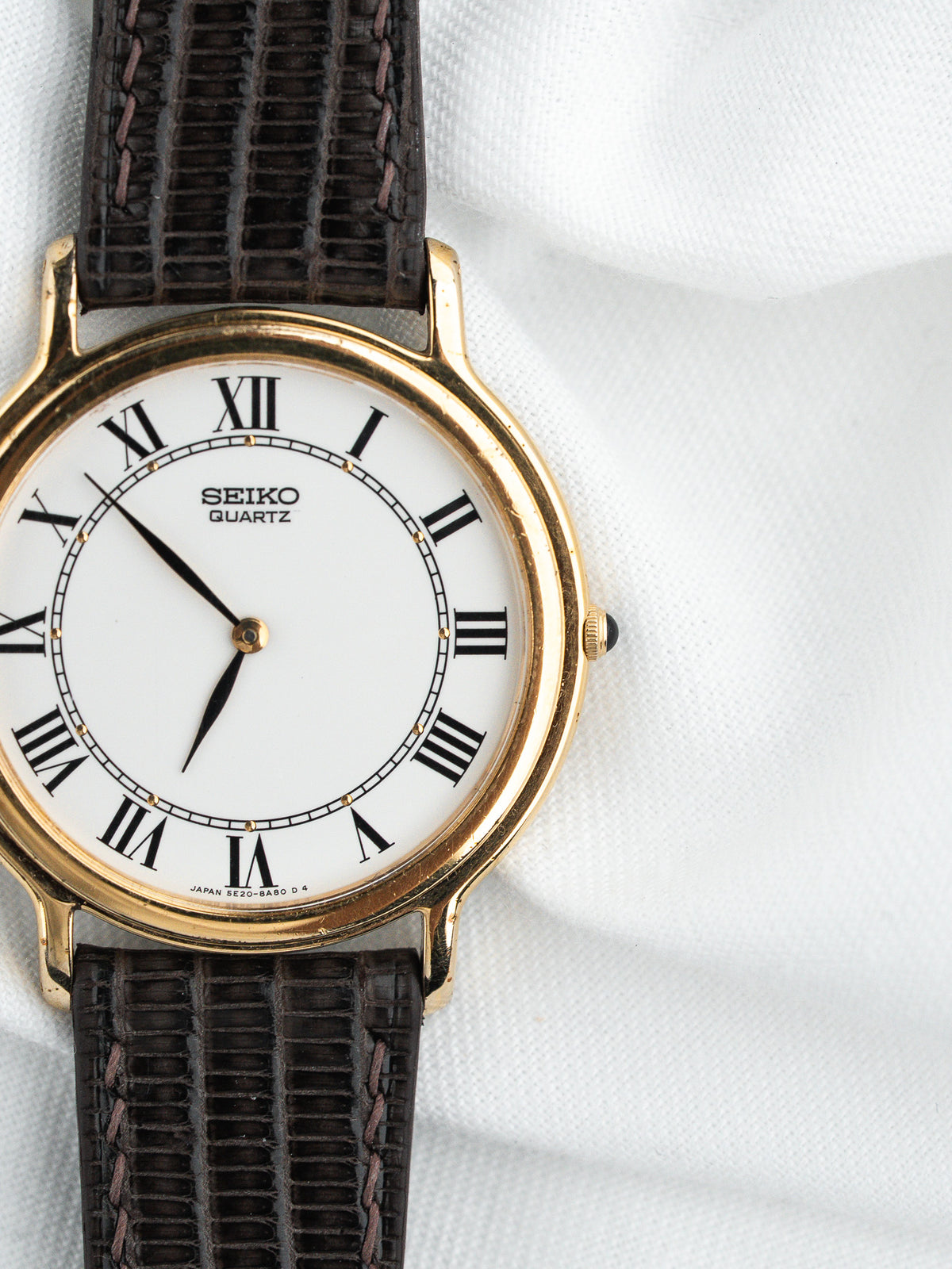 Montre Seiko Quartz vintage avec cadran blanc, chiffres romains et bracelet en cuir brun.