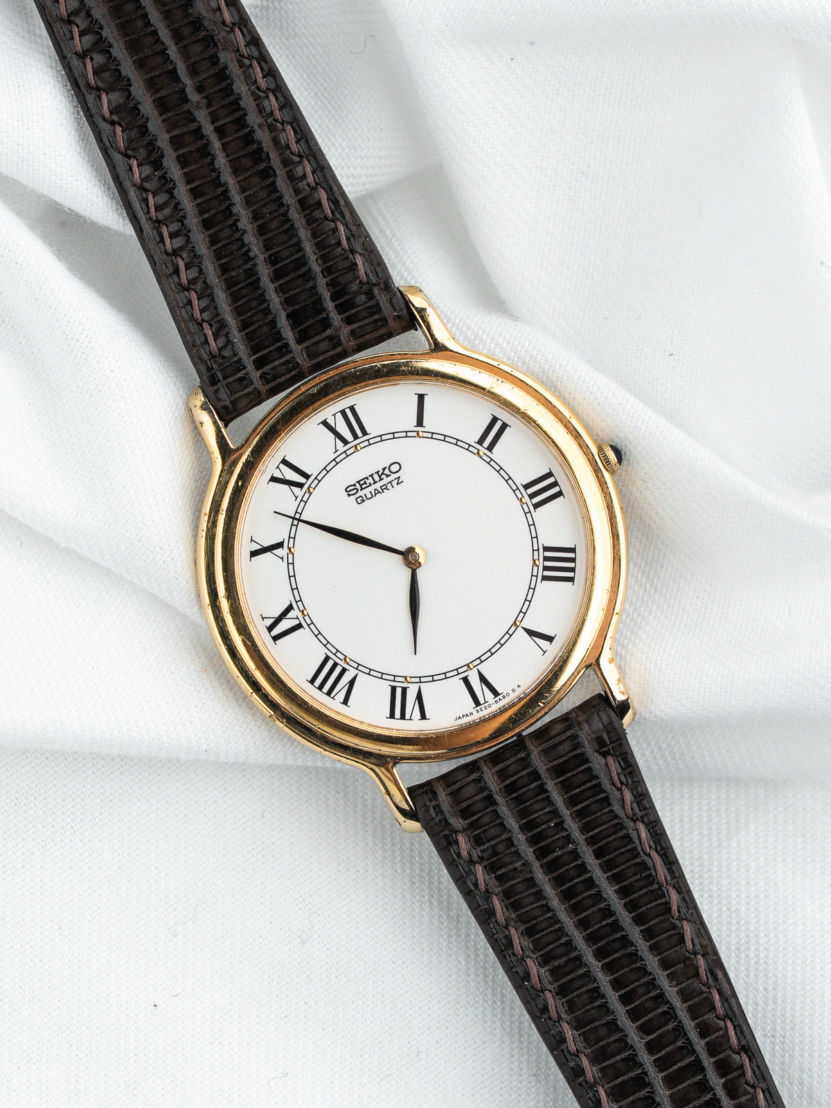 Montre Seiko Quartz vintage avec cadran blanc, chiffres romains et bracelet en cuir brun.