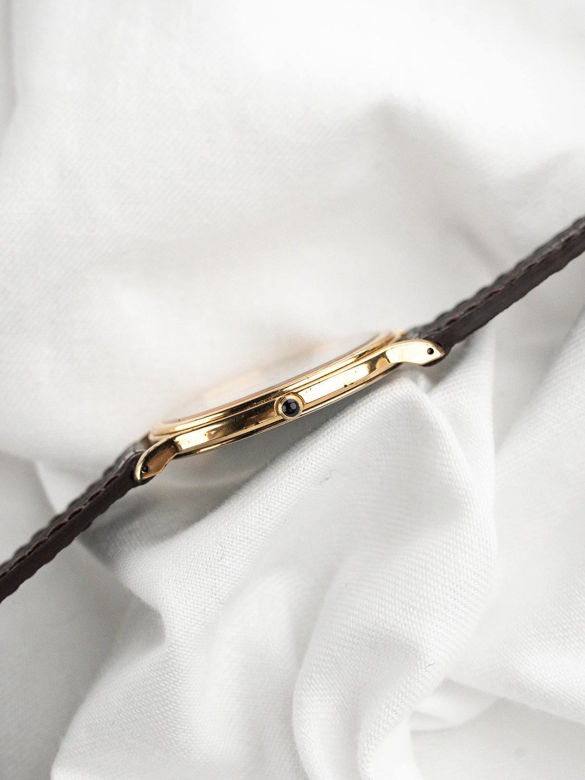 Vue de profil d'une montre au boîtier doré et bracelet en cuir marron.
