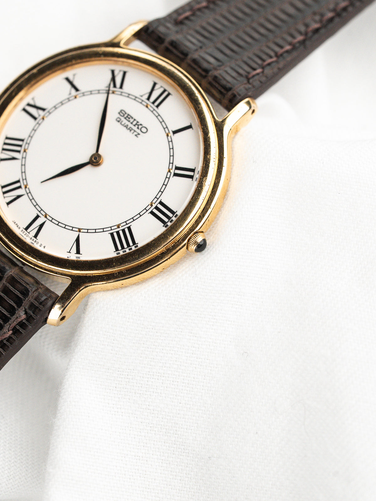 Montre Seiko Quartz vintage avec cadran blanc, chiffres romains et bracelet en cuir brun.