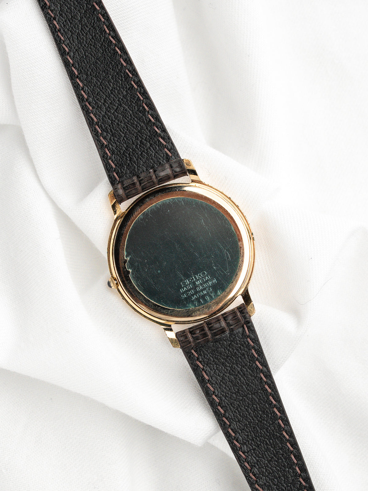 Vue arrière d'une montre vintage dorée avec un bracelet en cuir noir grainé.
