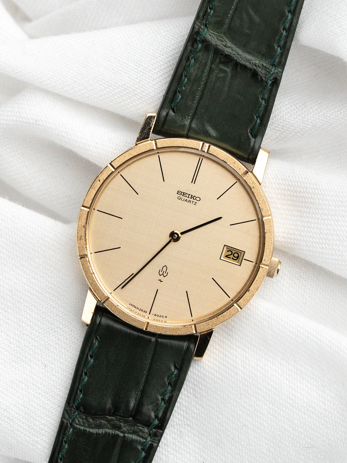 Montre Seiko Quartz vintage au cadran doré et bracelet en cuir vert foncé.