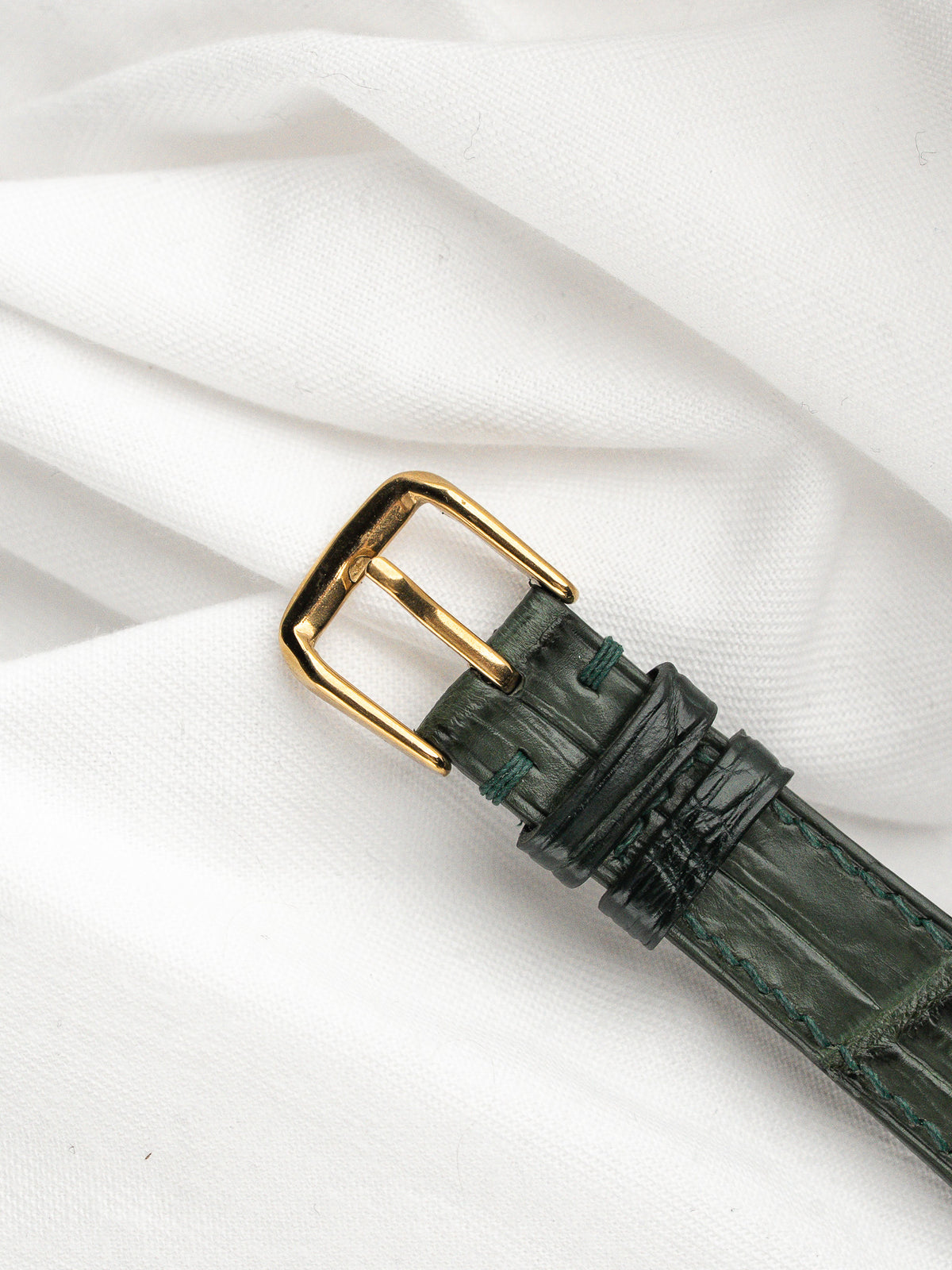 Détail d'une boucle dorée sur un bracelet de montre en cuir vert crocodile.
