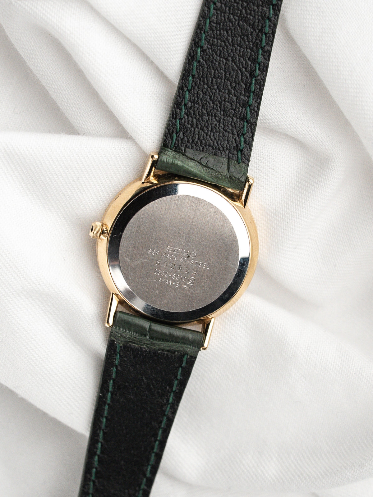 Dos d'une montre vintage avec boîtier doré et bracelet en cuir vert foncé.