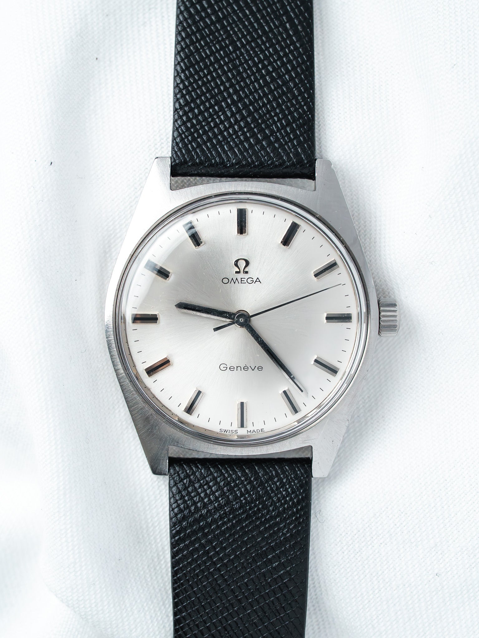 Omega Genève vintage watch with silver dial, black strap, and steel case on white background