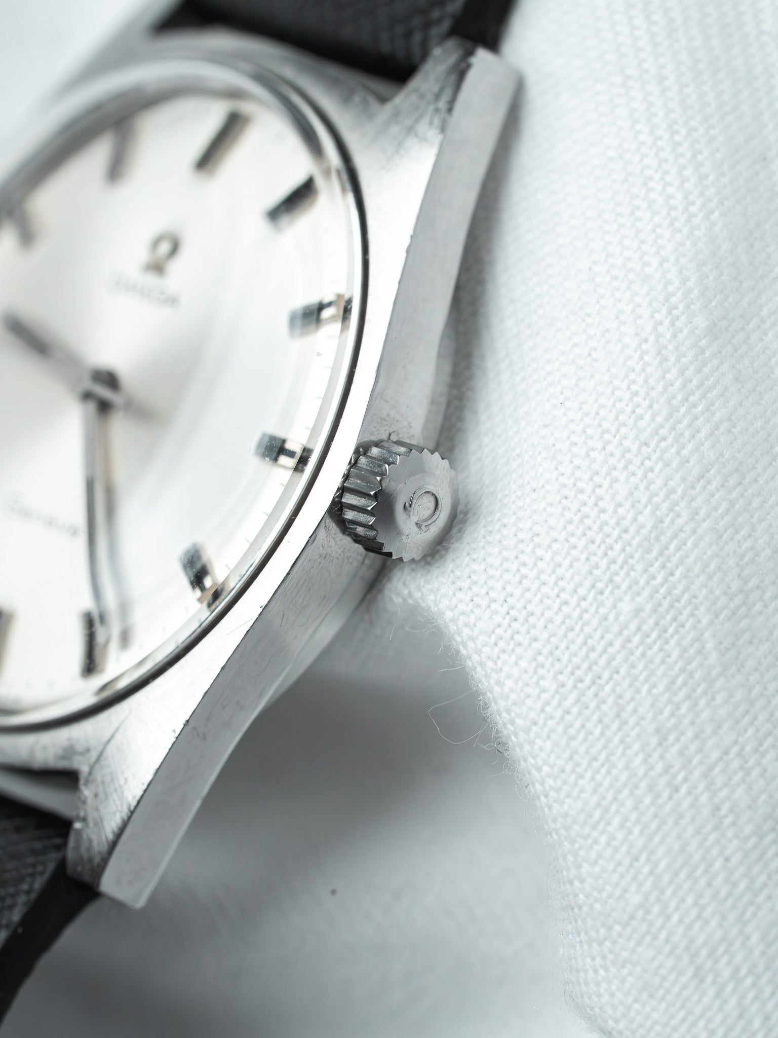 Vintage Omega watch with silver dial, black strap, and textured crown on white fabric