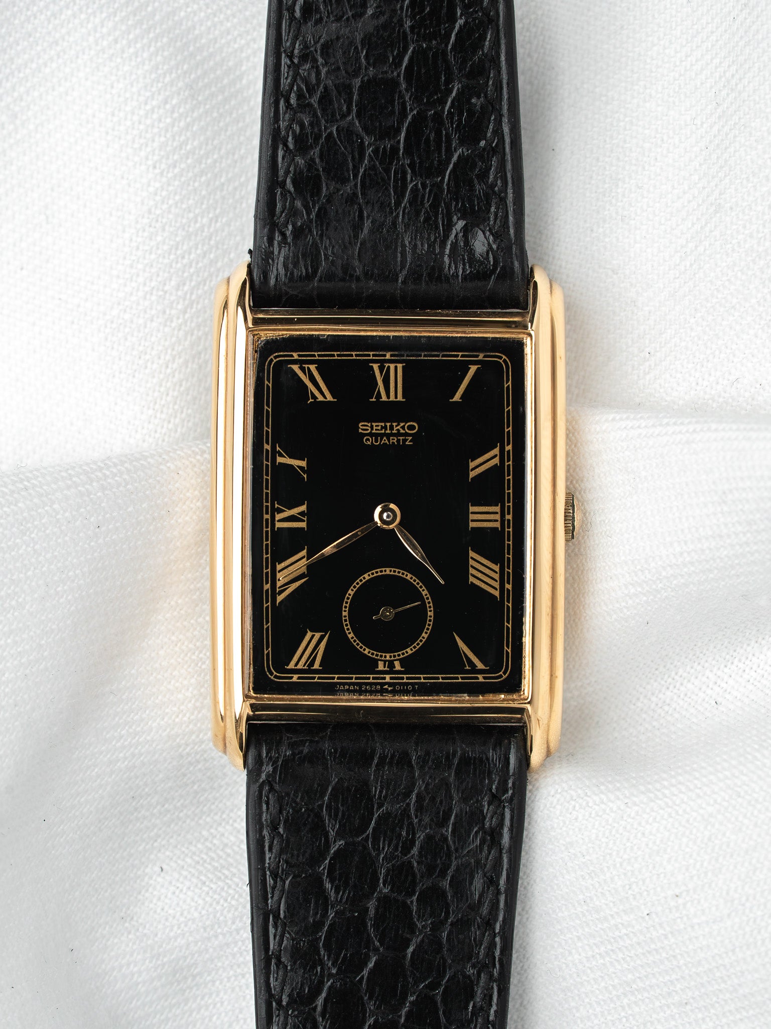 Seiko Quartz vintage watch with gold case, black dial, Roman numerals, and black textured strap