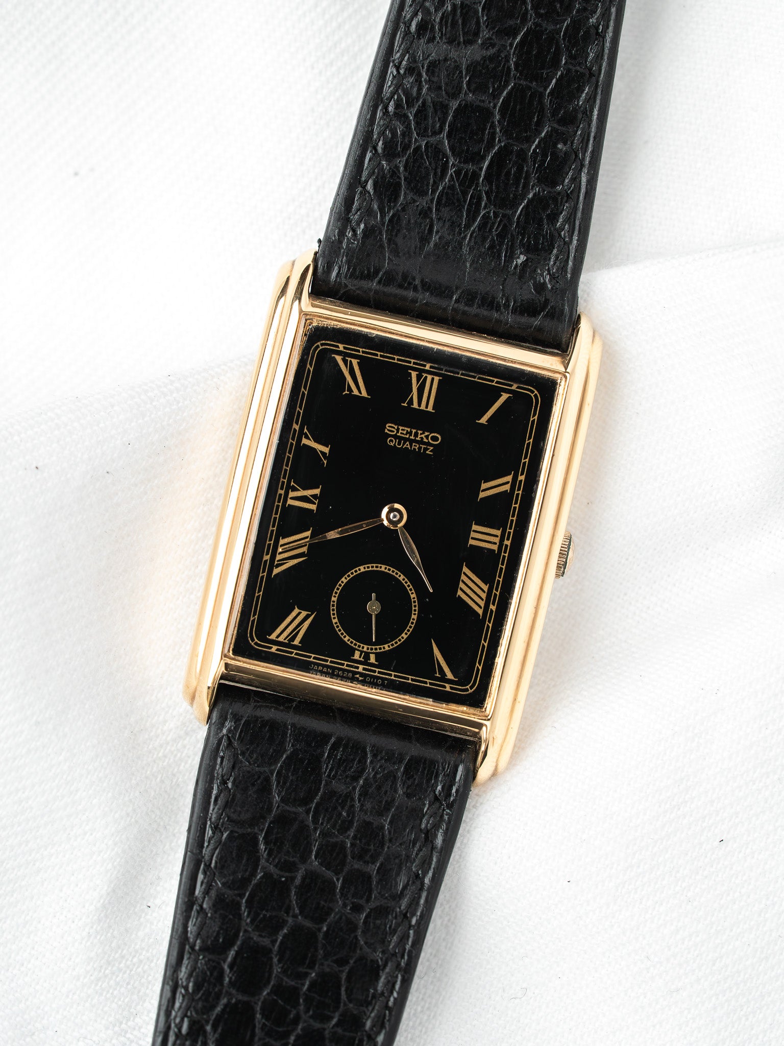 Seiko Quartz vintage watch with gold case, black dial, Roman numerals, and textured strap