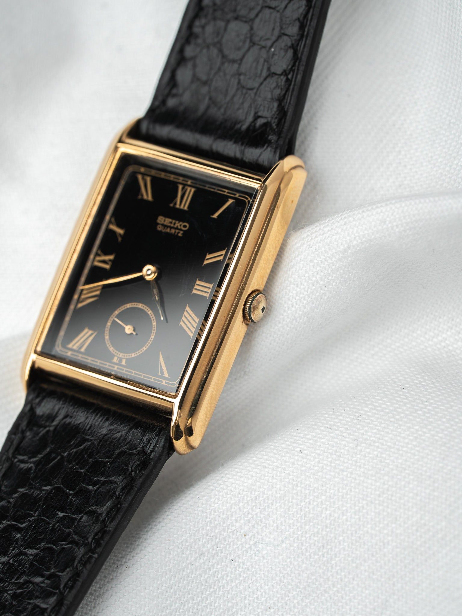 Seiko vintage quartz watch with gold case, black dial, Roman numerals, and black leather strap
