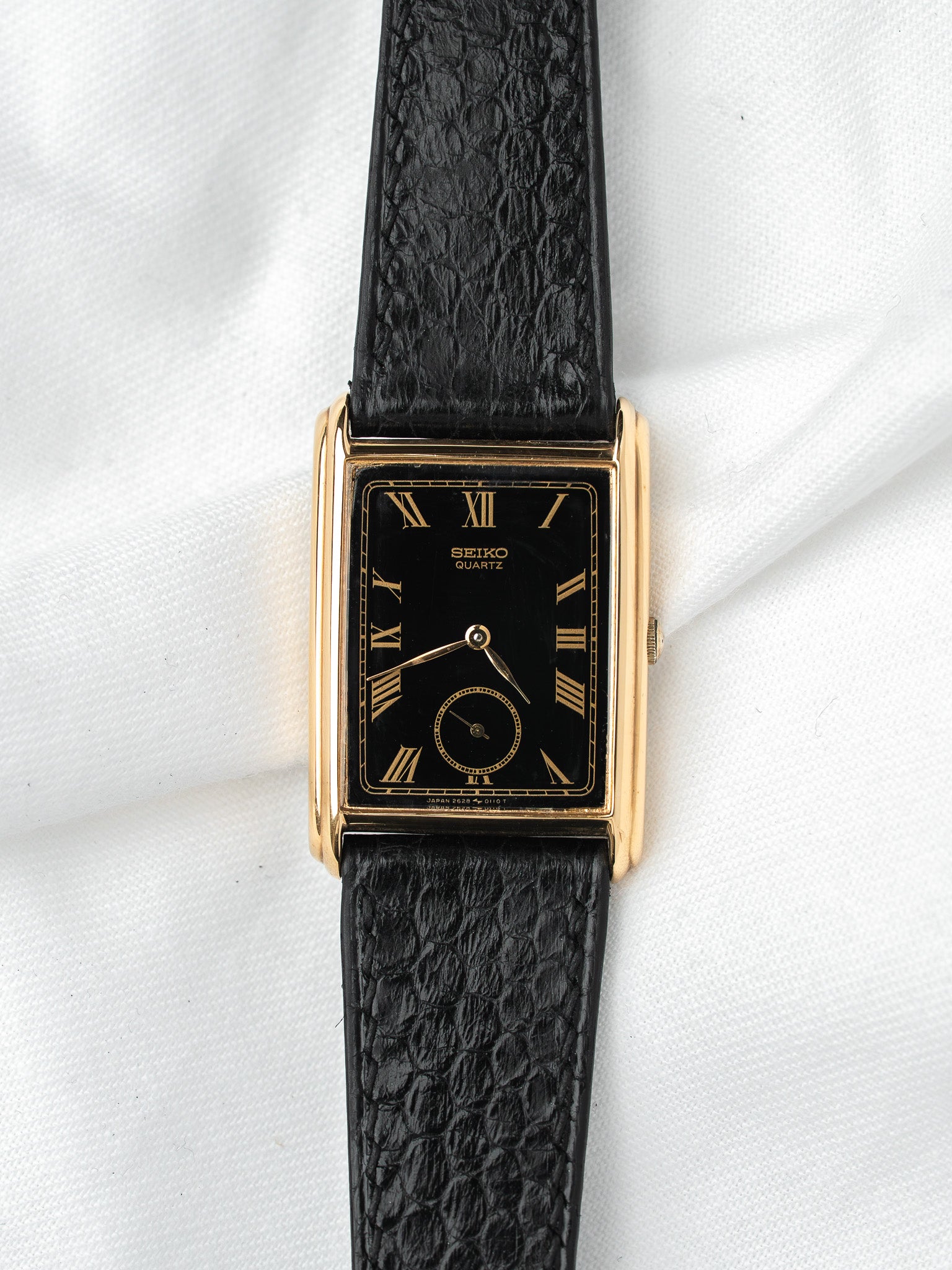 Seiko Quartz vintage watch with gold case, black dial, Roman numerals, and textured strap