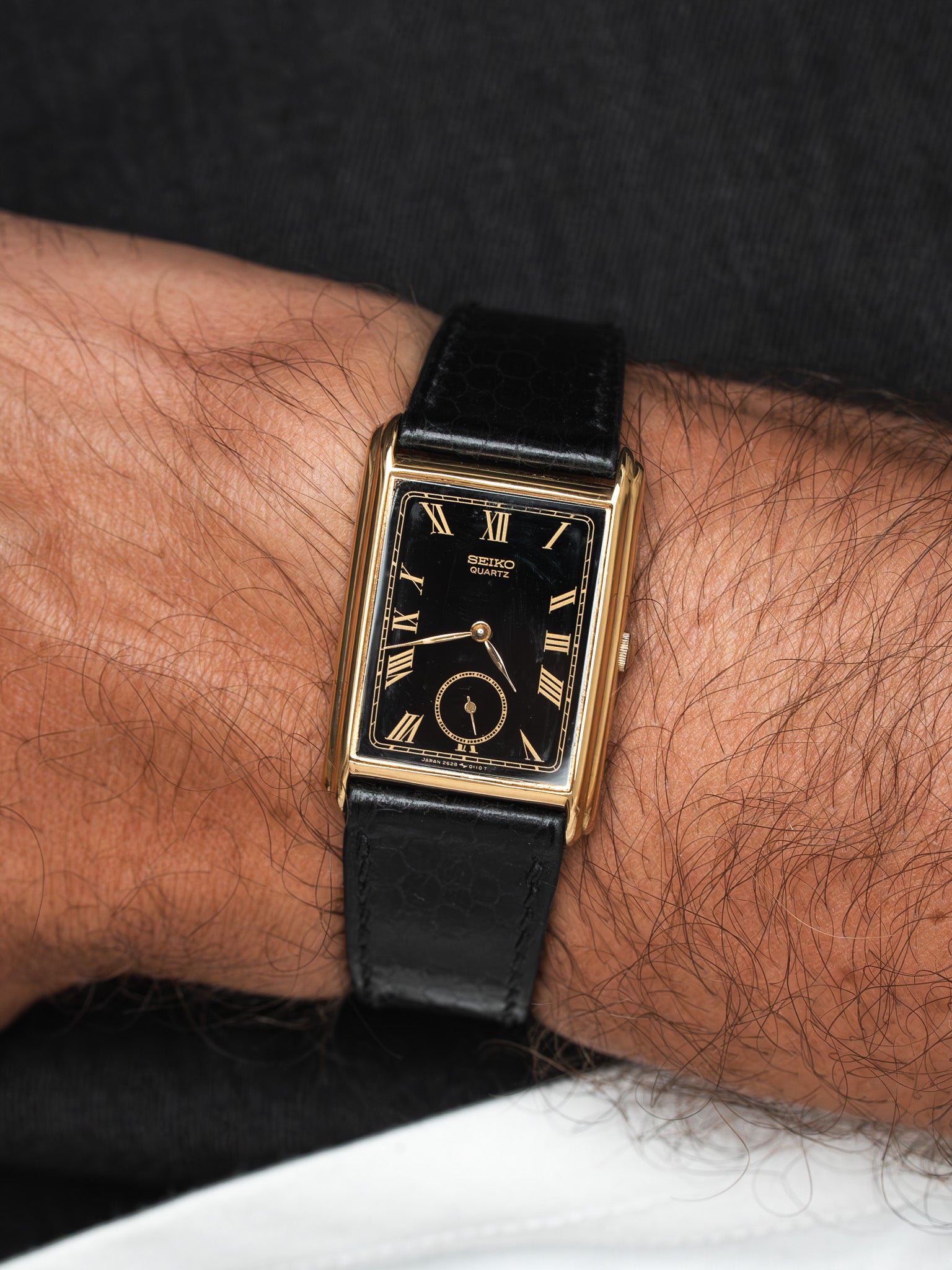 Seiko quartz vintage watch with gold case, black dial, Roman numerals, worn on wrist