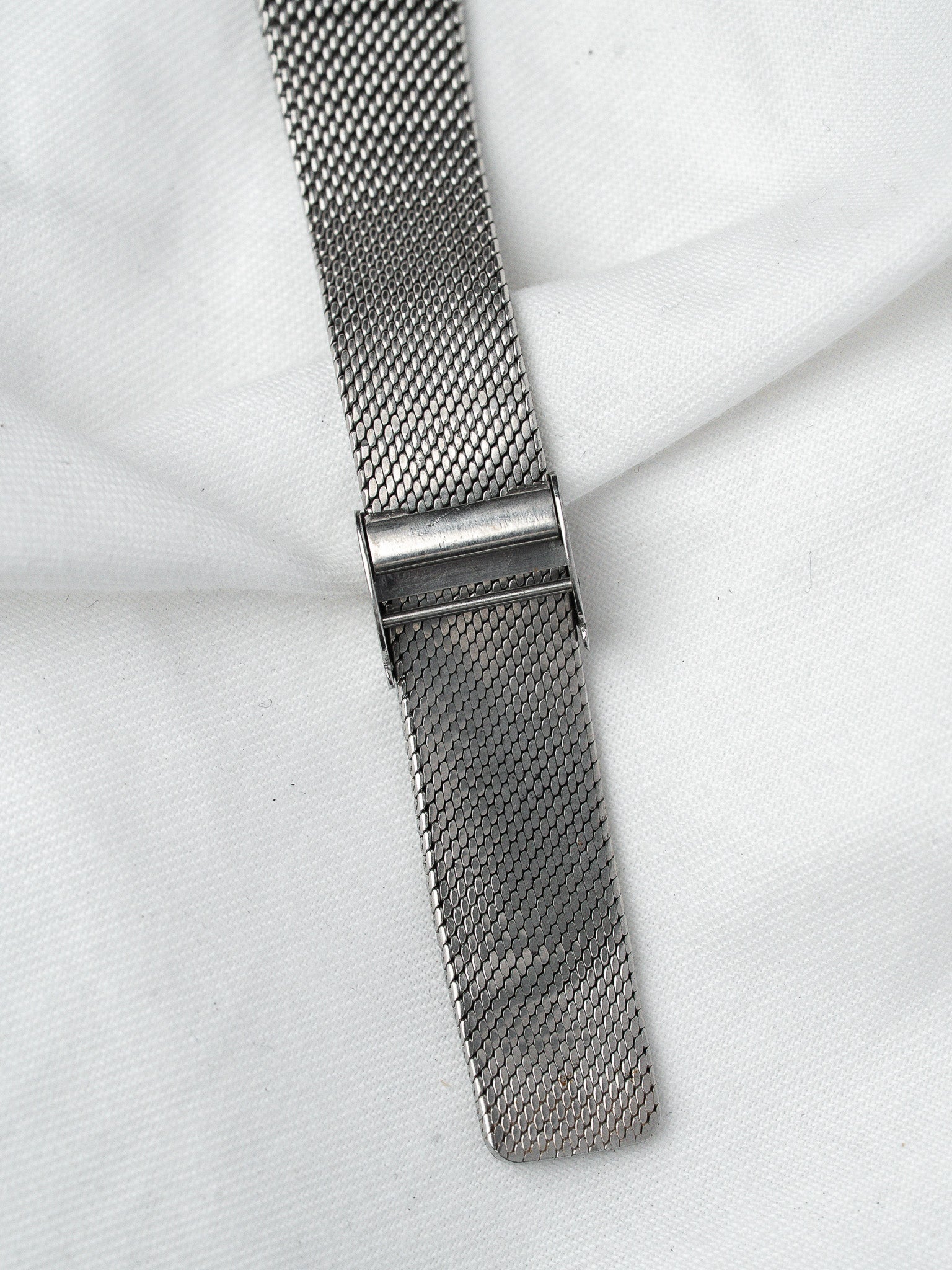 Vintage mesh watch strap in stainless steel, detailed clasp on white fabric