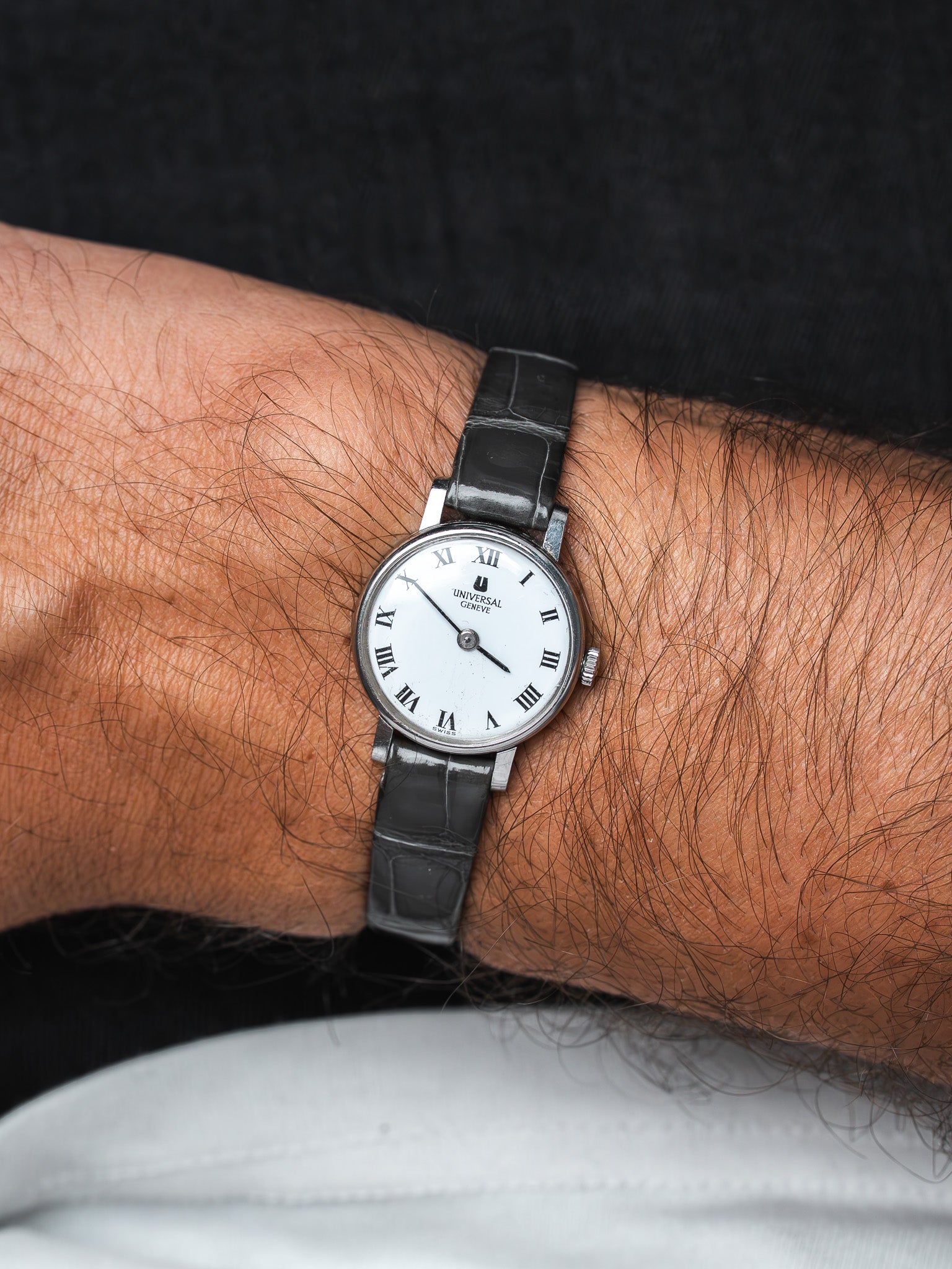 Universal Genève vintage watch with white dial, Roman numerals, black leather strap on wrist