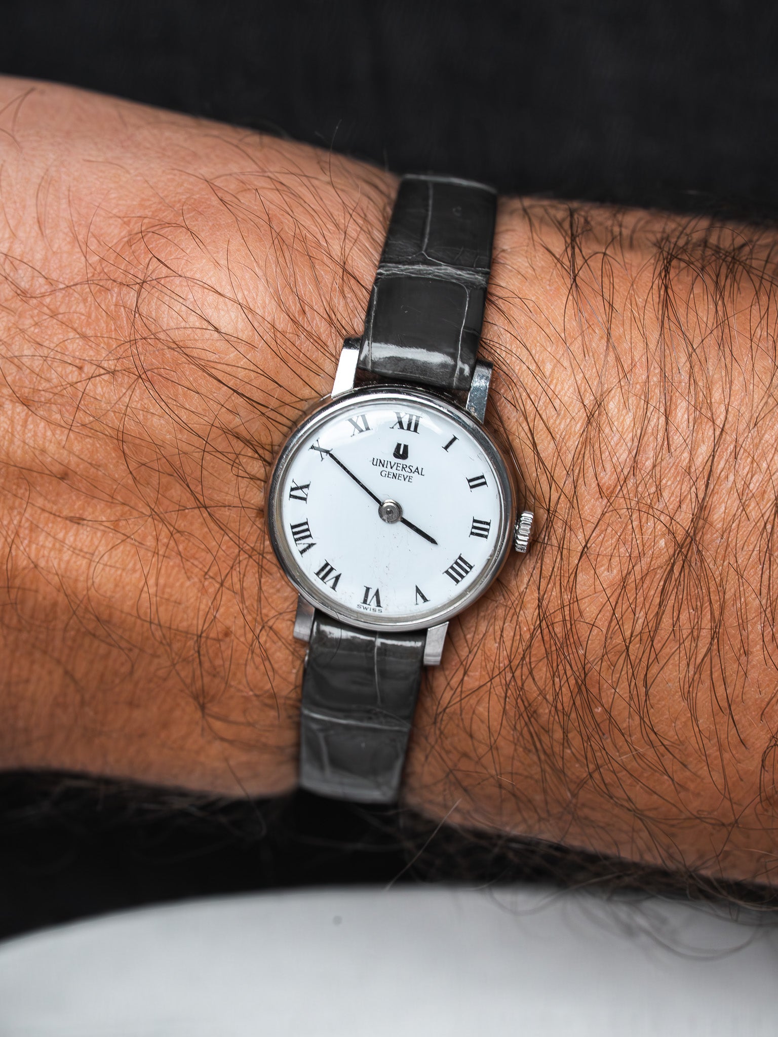 Universal Genève vintage watch with white dial, Roman numerals, black leather strap on wrist